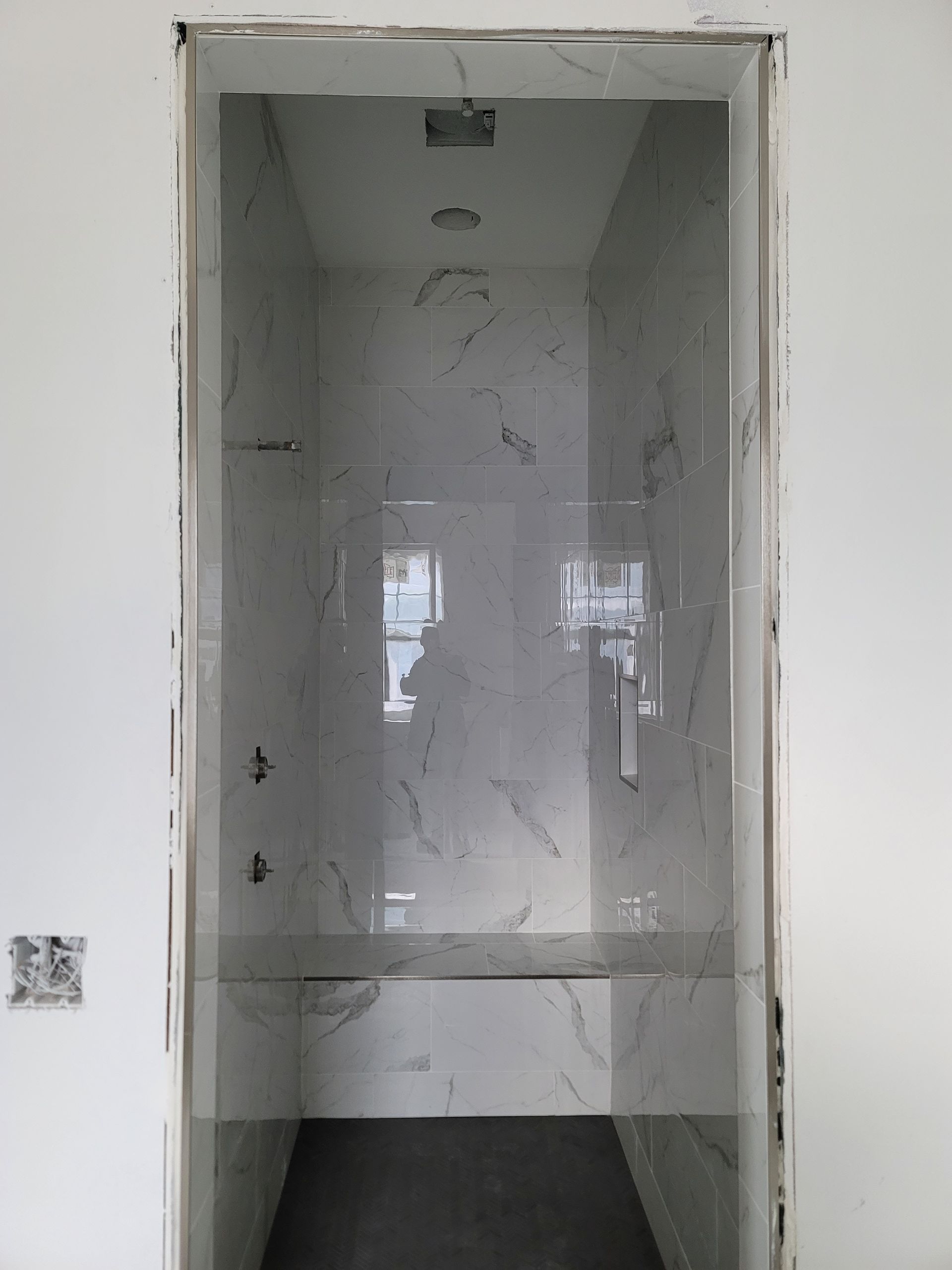 Empty white wall cabinet niche with shelves and reflective back panel, unfinished interior drywall opening