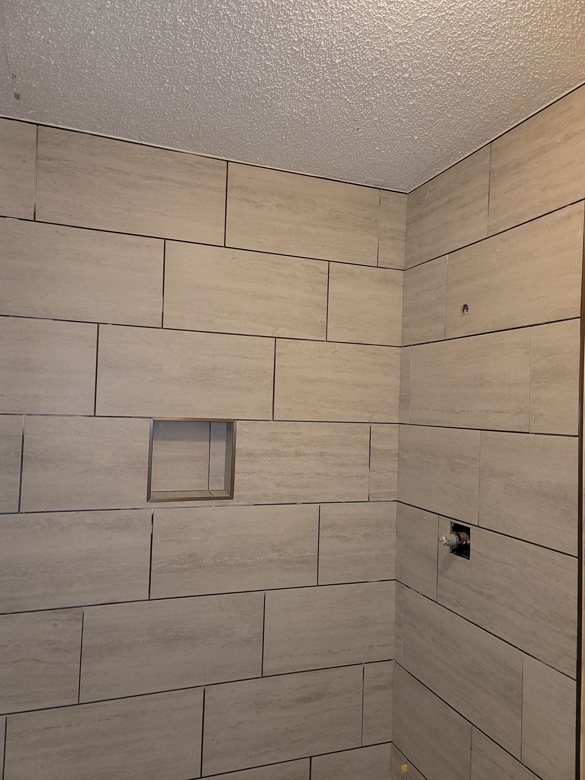 Partially tiled shower wall with a small recessed niche and a protruding pipe opening
