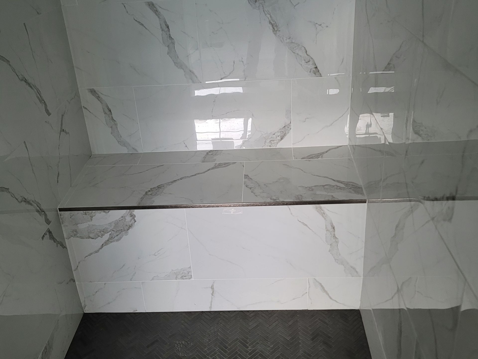 White marble-tiled wall with a dark horizontal strip and a gray tiled floor corner