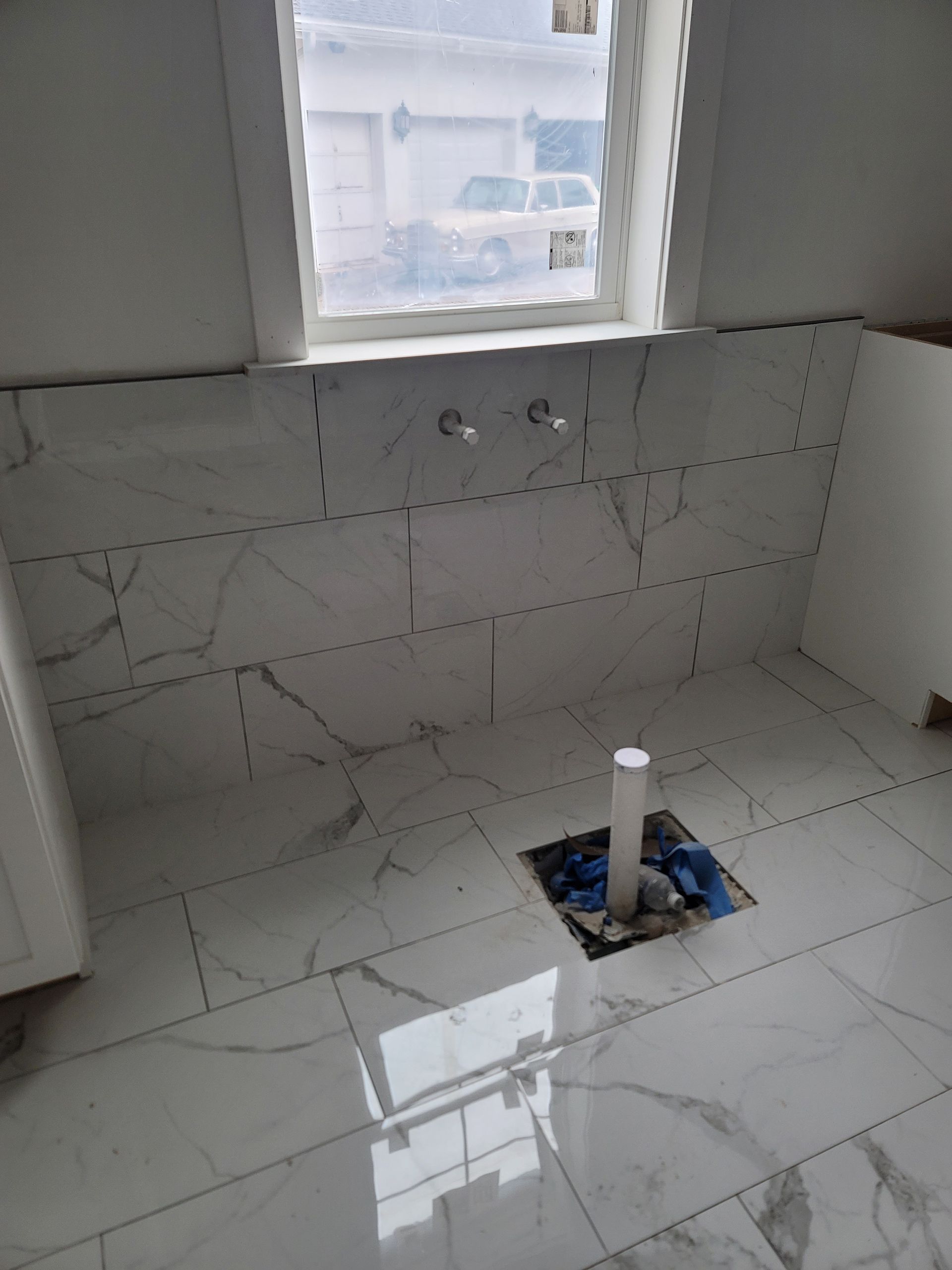 Empty tiled kitchen under construction with a sink opening in the floor and a window above the backsplash.