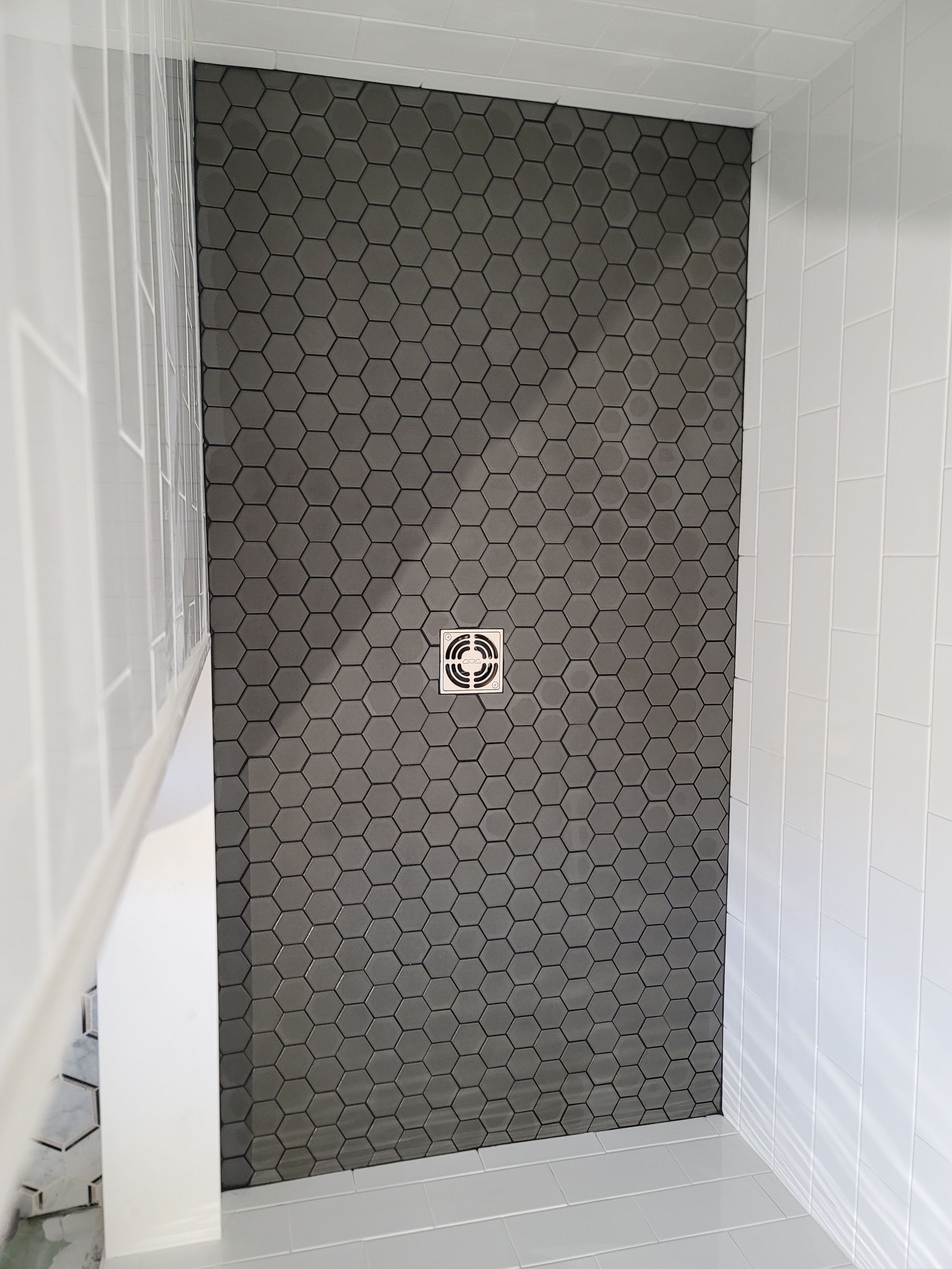 Stairwell with patterned gray tile wall and a floor drain, framed by white walls and stairs
