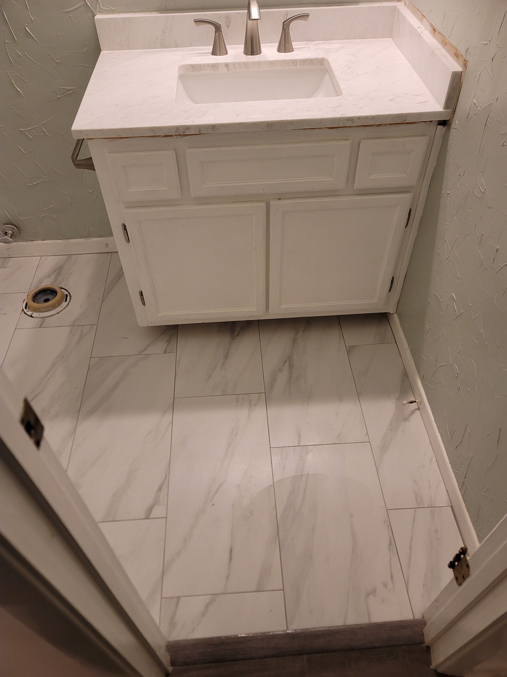 Small bathroom with white vanity sink and marble-pattern floor tiles, viewed from the doorway