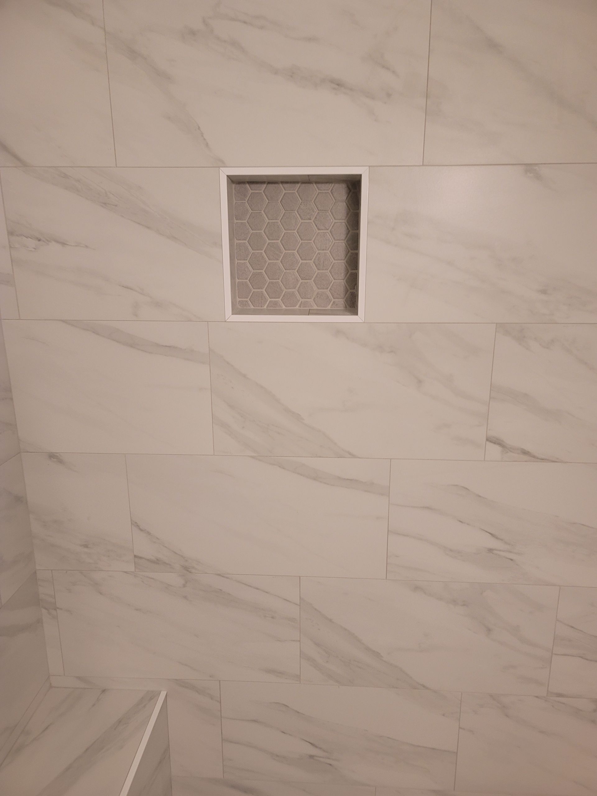 Marble-tiled shower wall with a small square frosted window near the top.