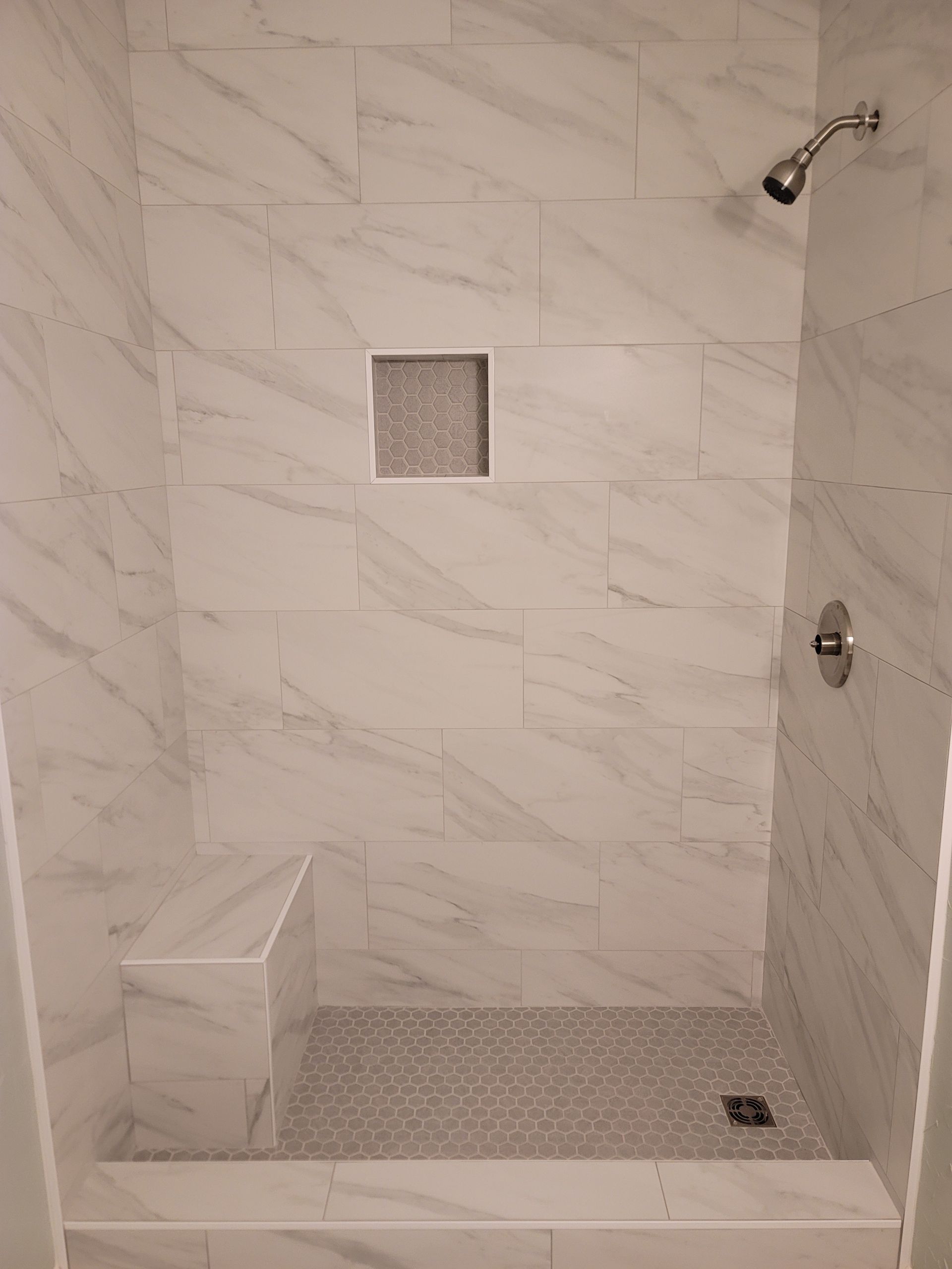 White tiled shower with bench, square niche, and chrome fixtures.