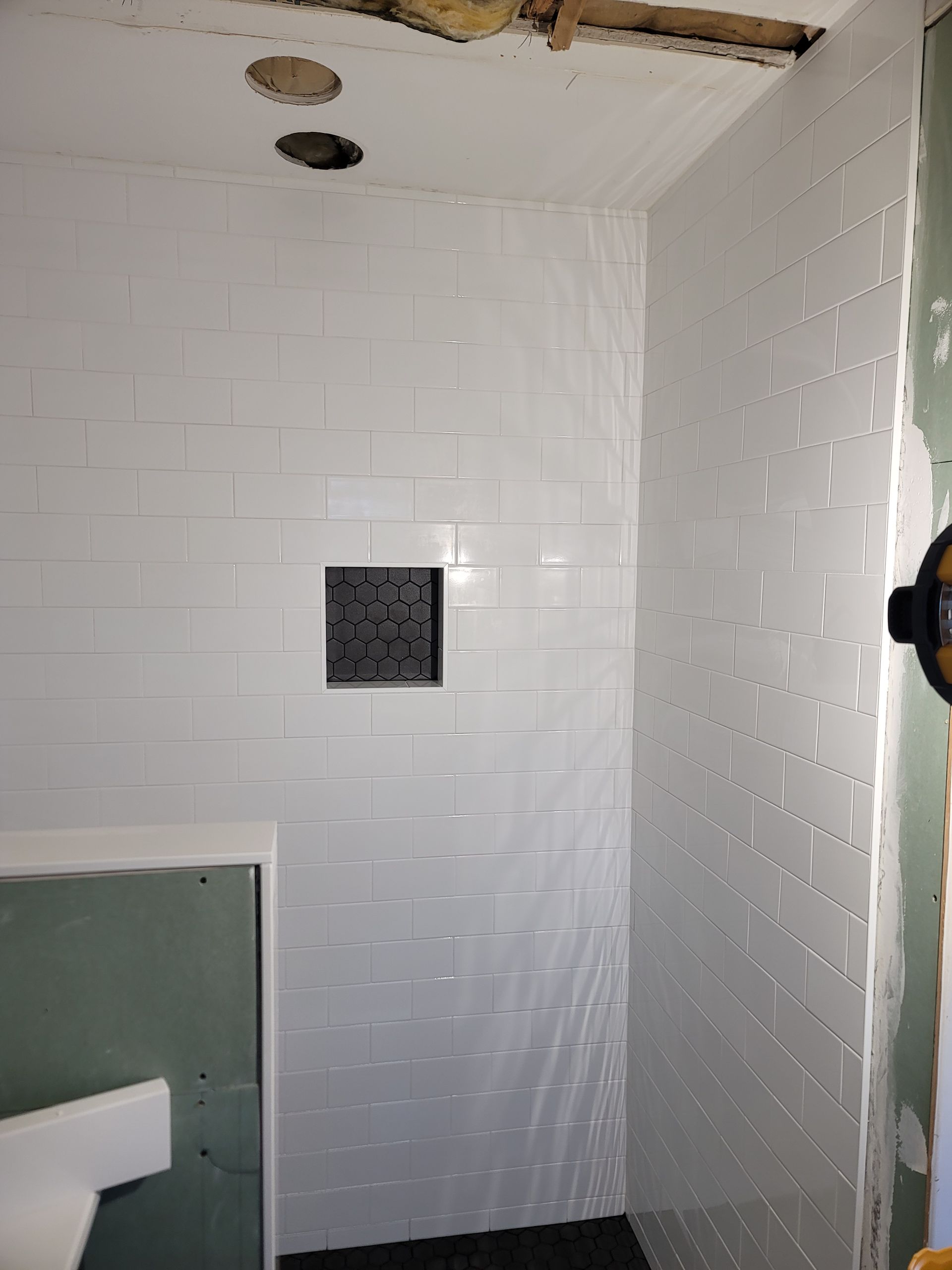 White tiled shower stall with a small square niche and exposed holes in the ceiling.