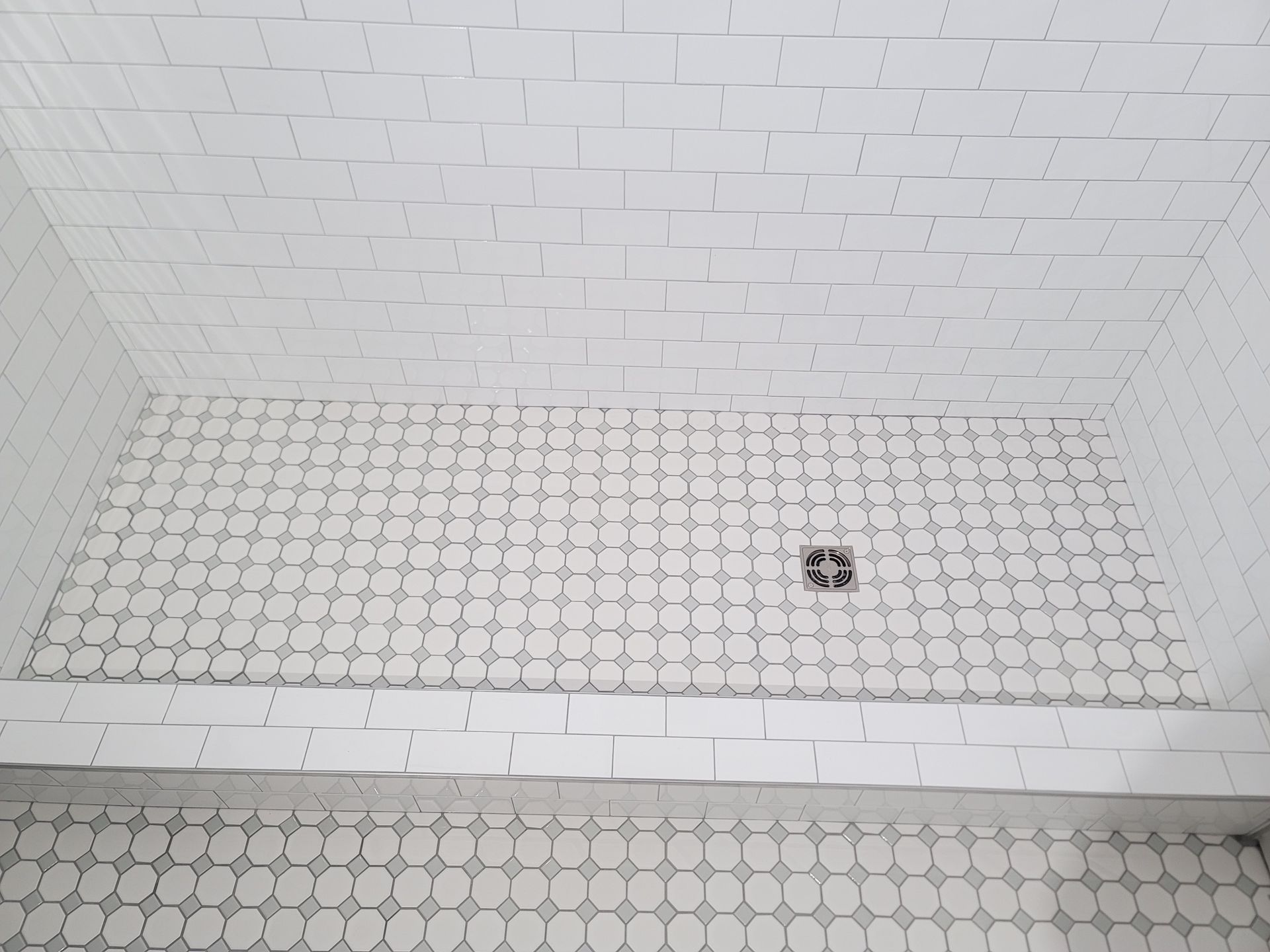 Empty white tiled shower with a small drain and soap dish.
