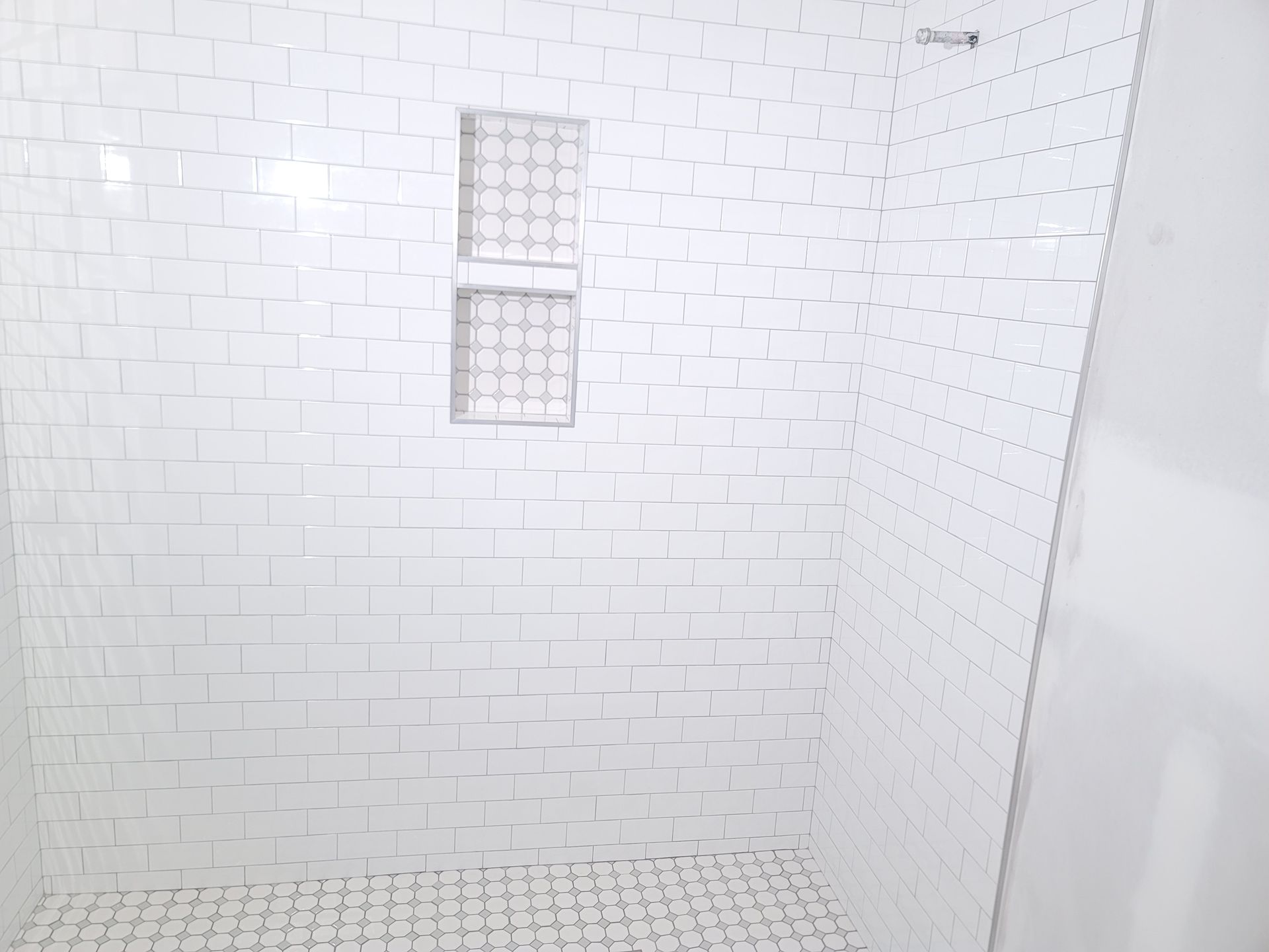 White tiled shower stall with a built-in soap niche and a shower floor drain.