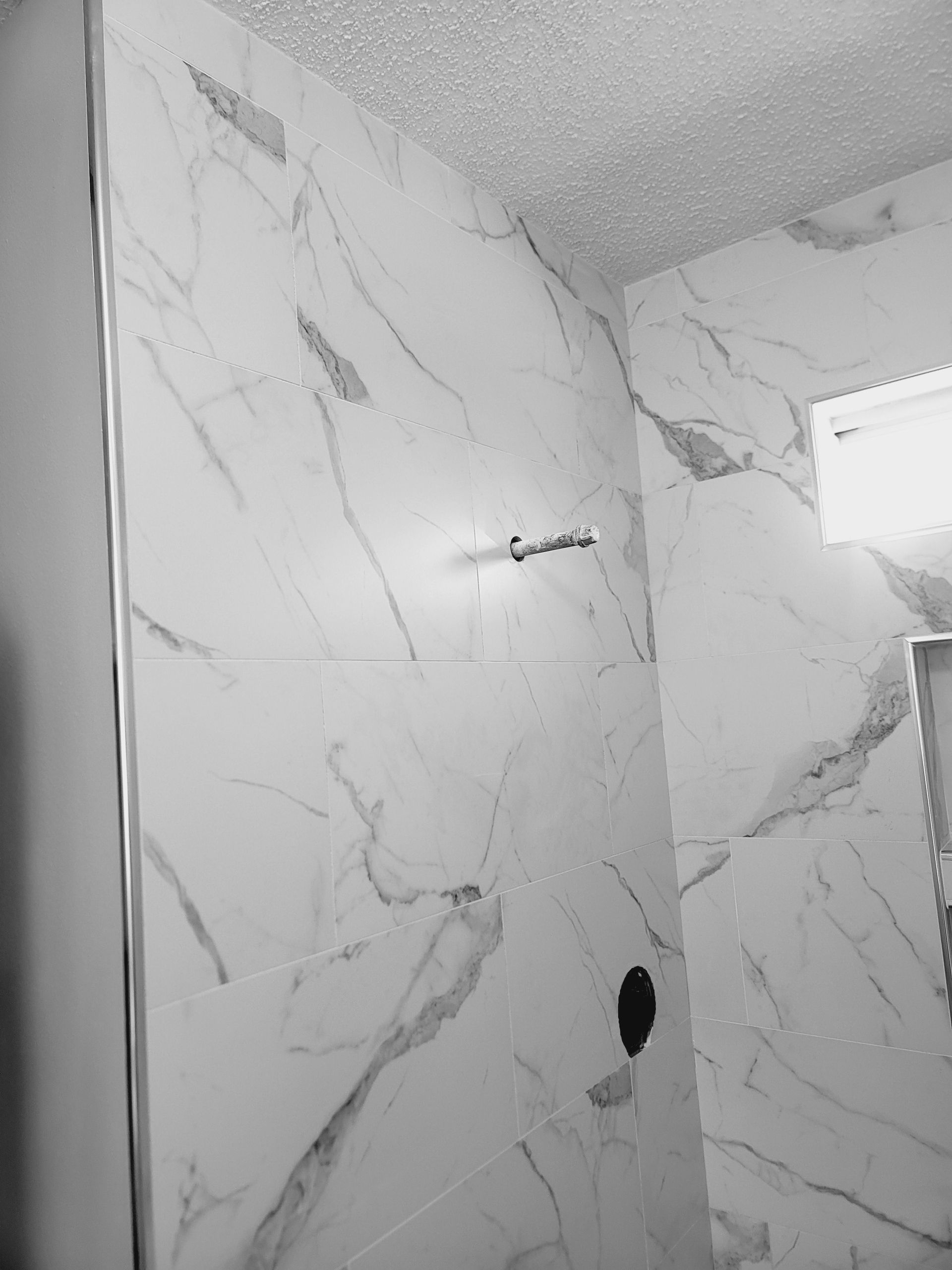 Marble-tile shower wall with a light fixture and rough cutout holes in the tile