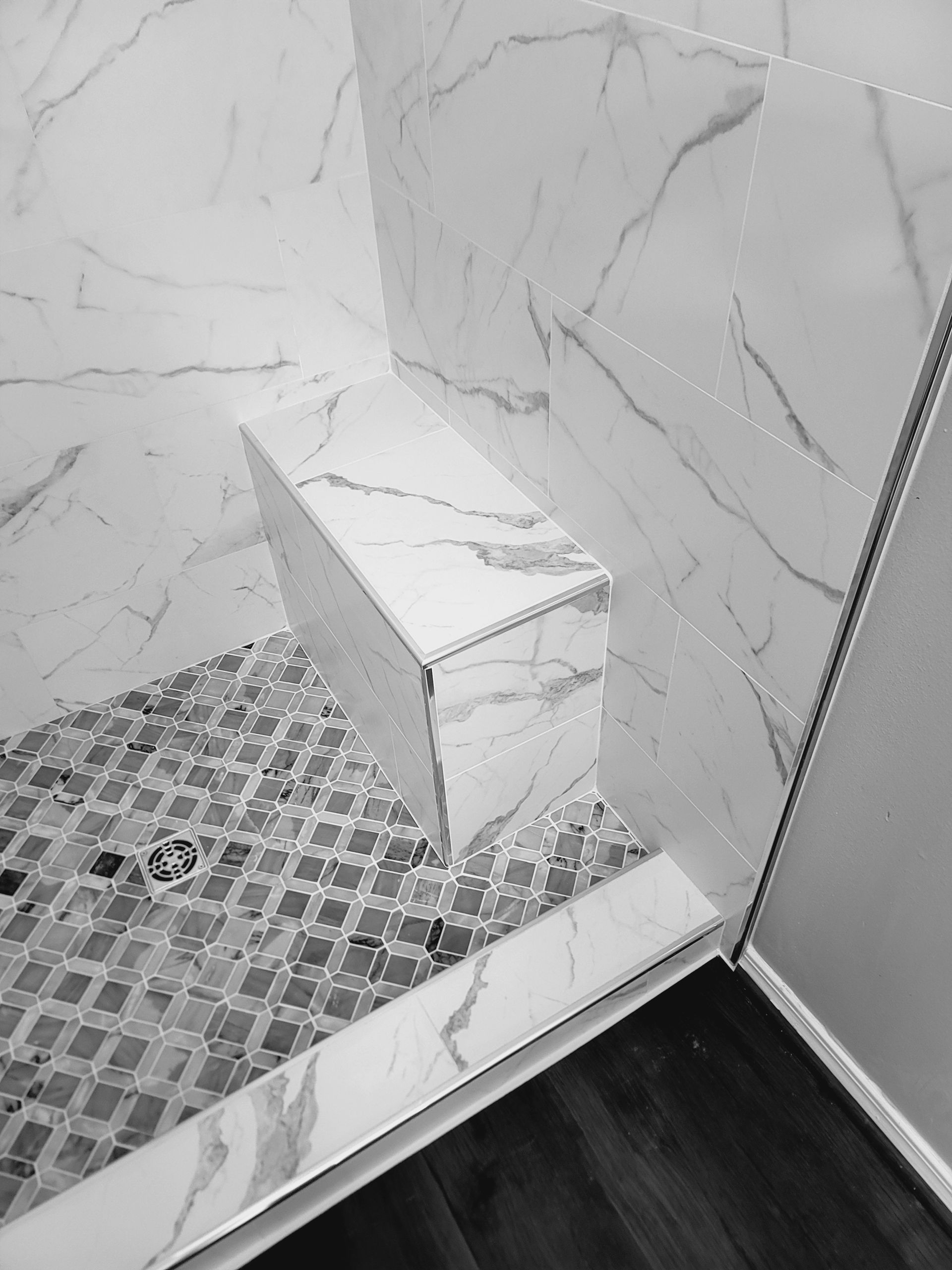 Tiled shower corner with built-in bench and marble-pattern wall panels above a mosaic floor.