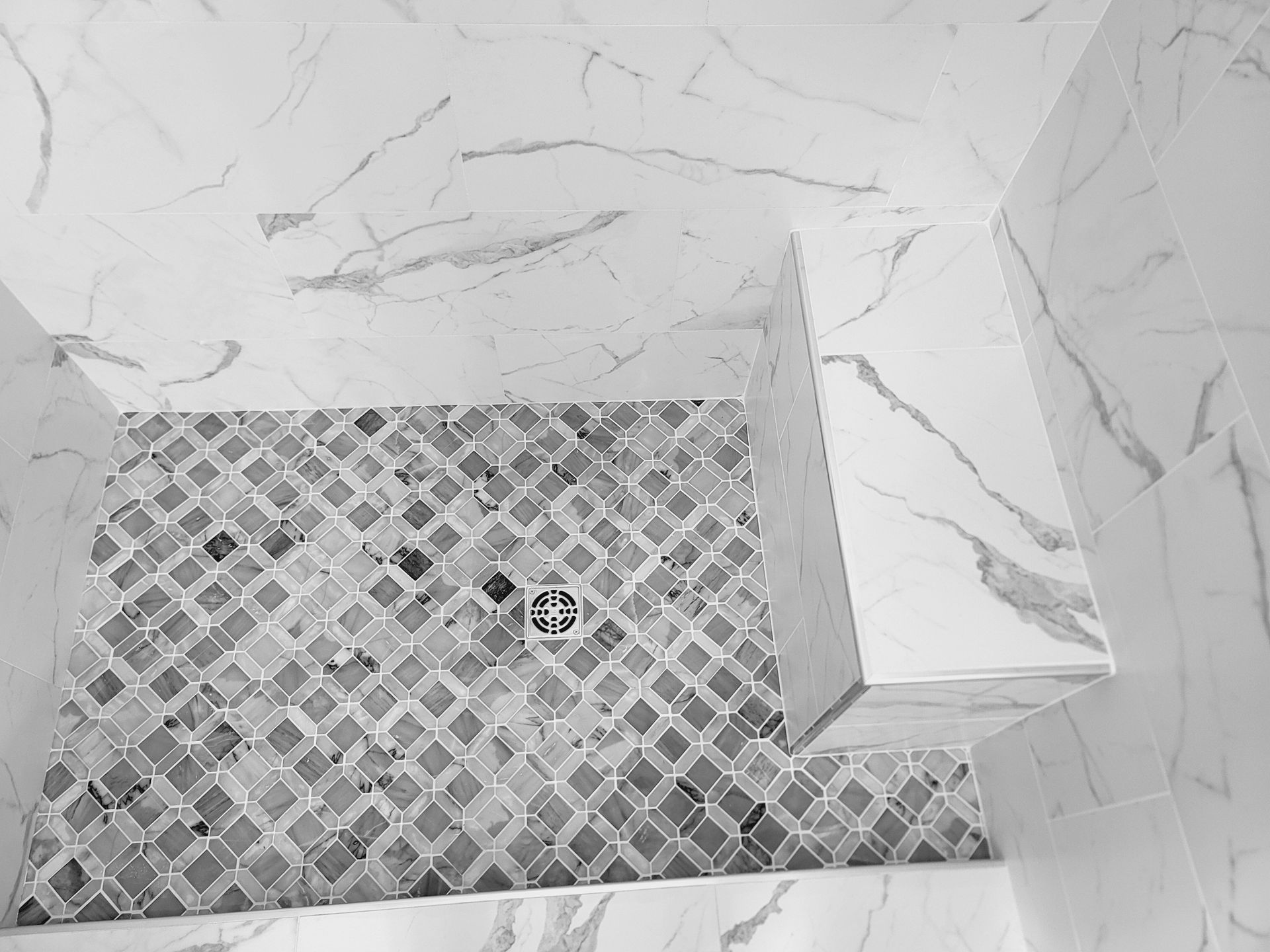 Tiled shower floor with a mosaic drain and marble-look wall tiles