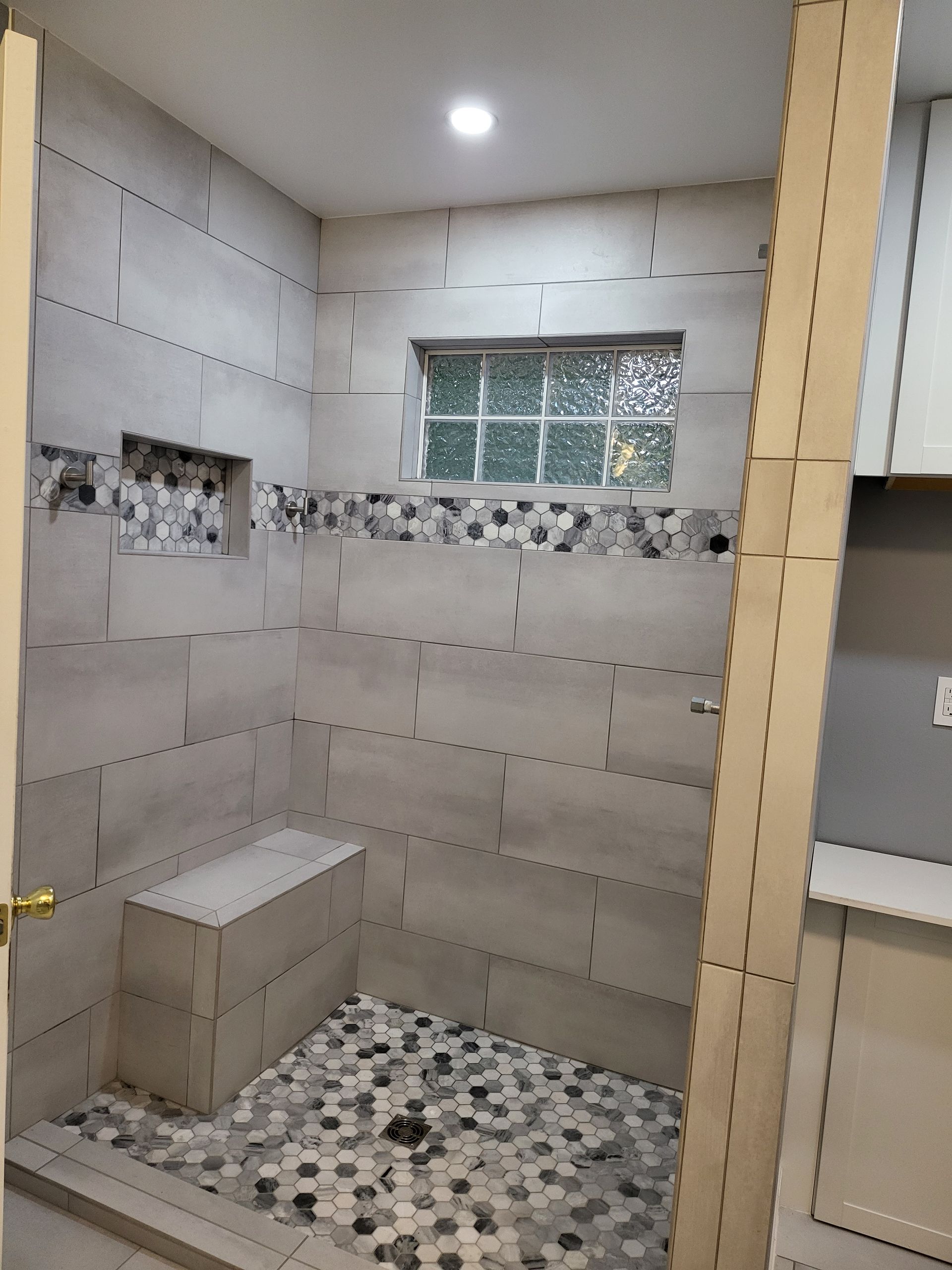 Partially tiled bathroom shower with pebble floor and small window, under construction
