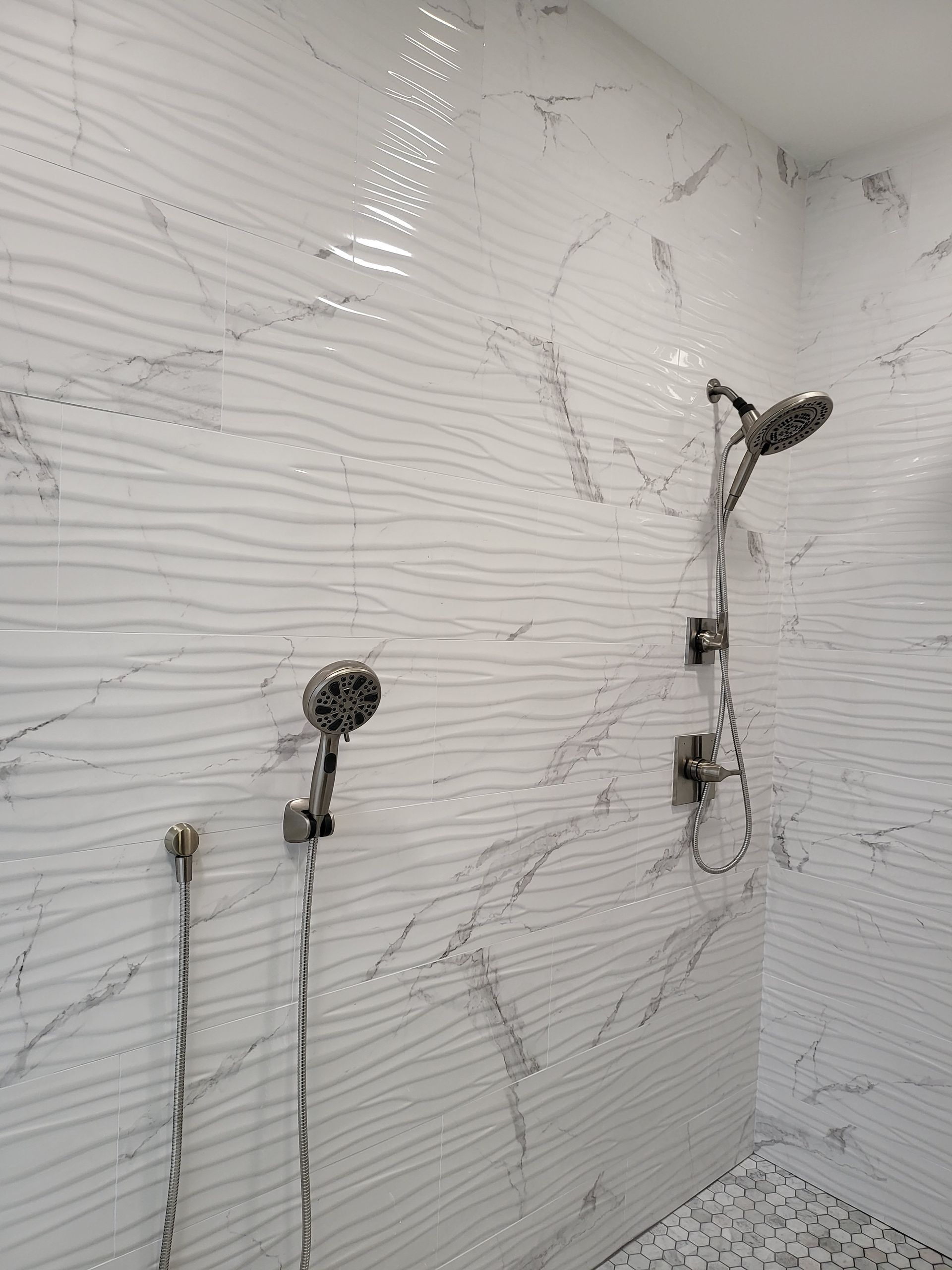 White tiled shower wall with exposed plumbing fixtures and rough patching marks.