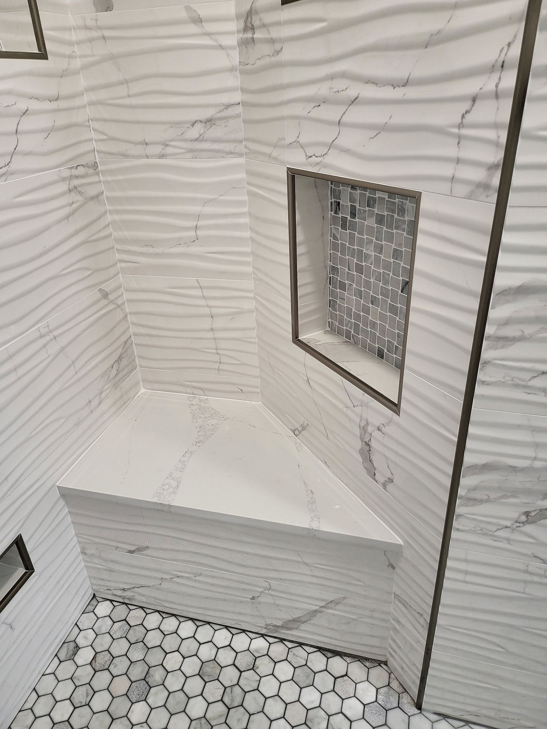 White tiled bathroom shower with hex tile floor, built-in bench, and a small recessed window.