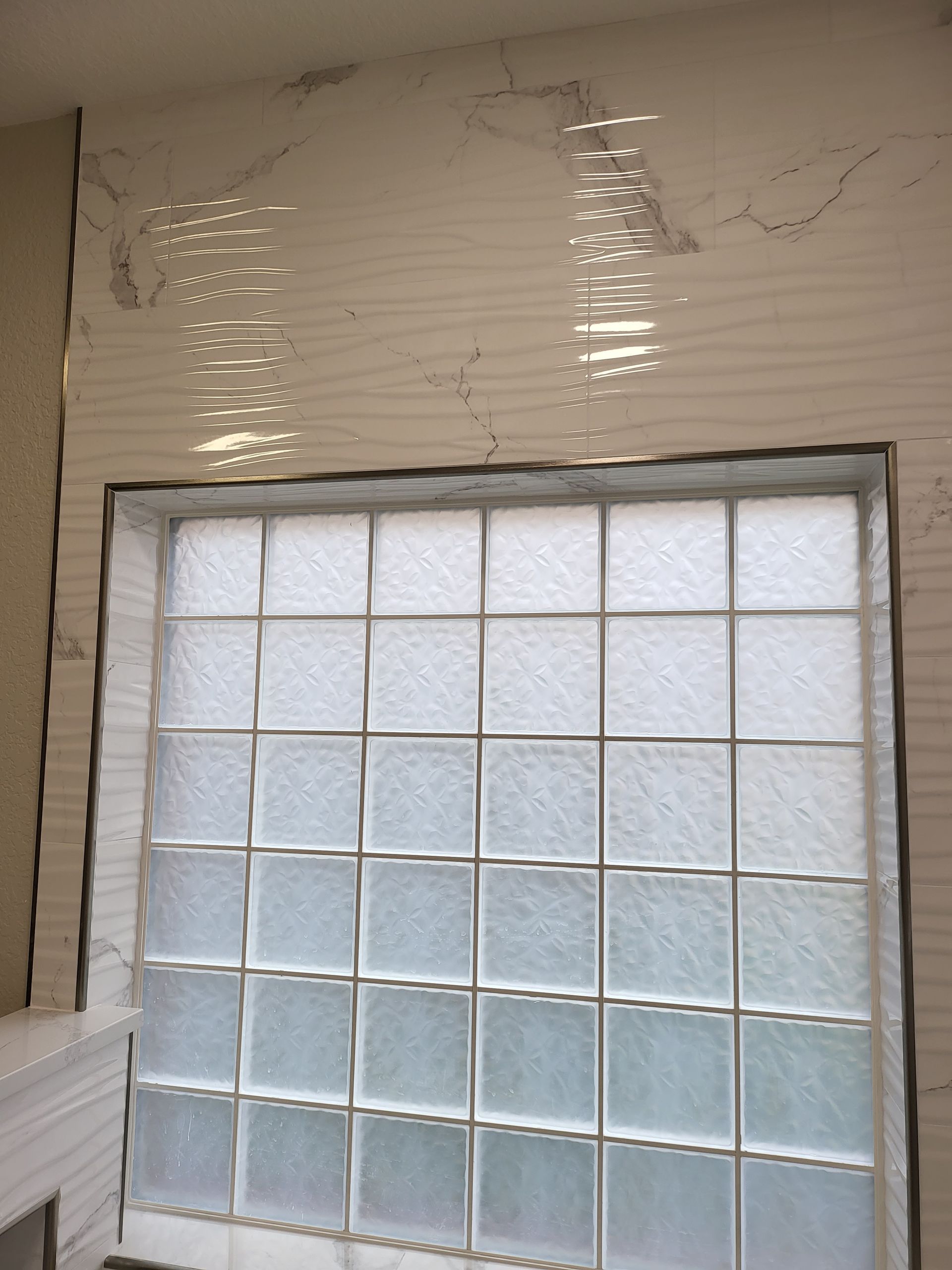 Frosted glass block window in a white tiled wall with water damage and peeling paint above it