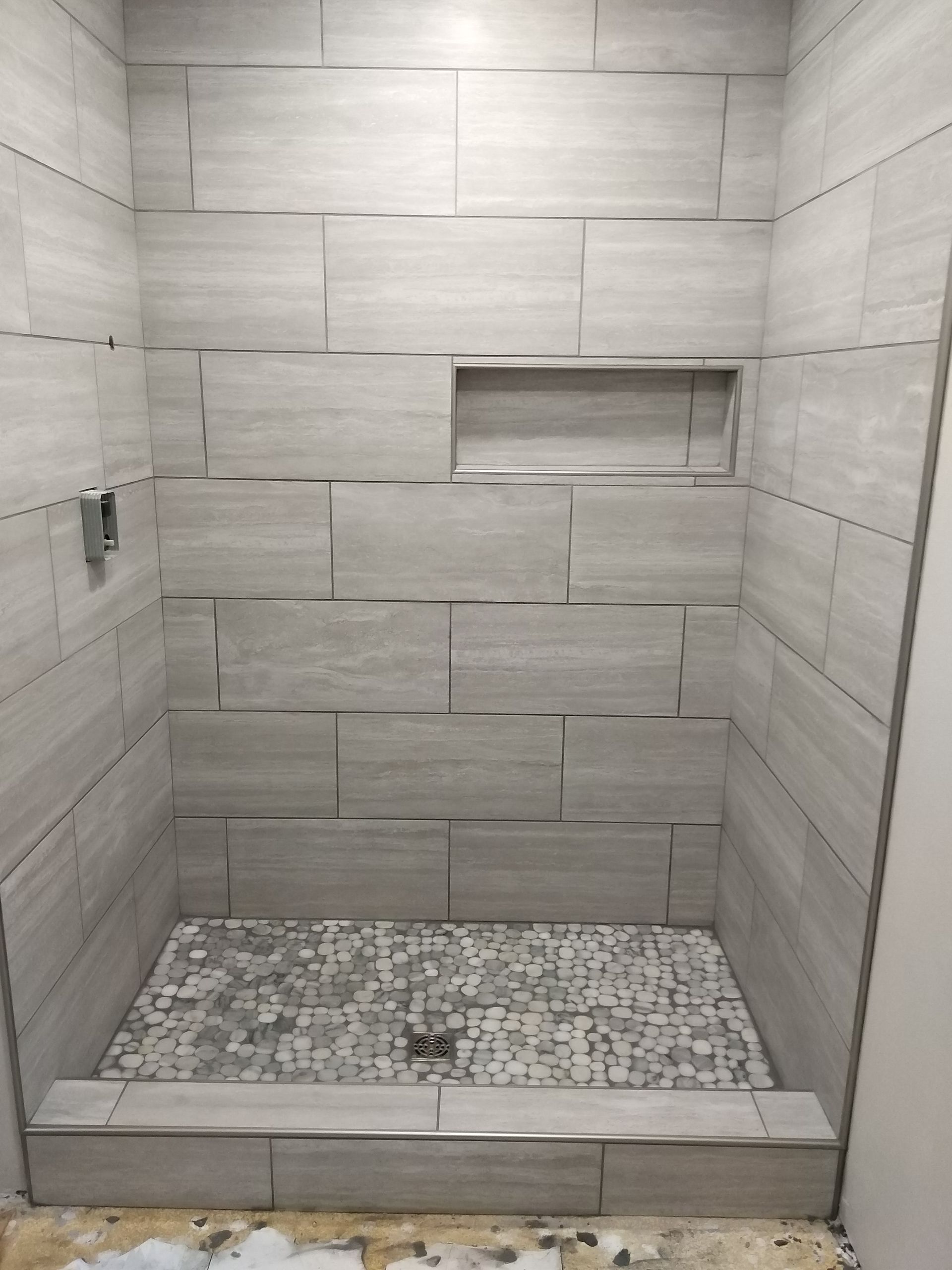 Modern tiled shower with a pebble floor, built-in niche, and low step-in curb