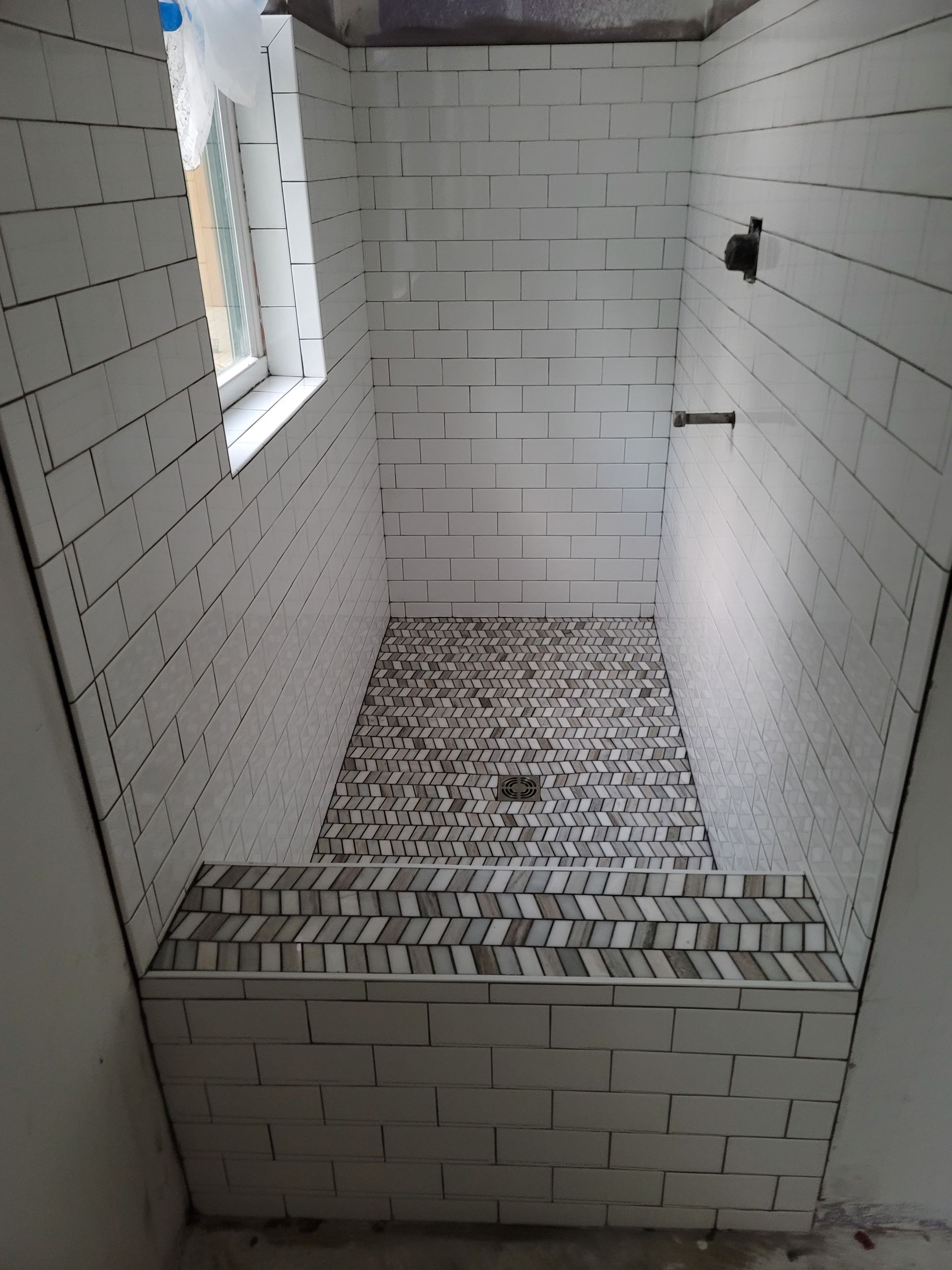 Small tiled bathroom with a shower stall, white subway tiles, and a window on the left.