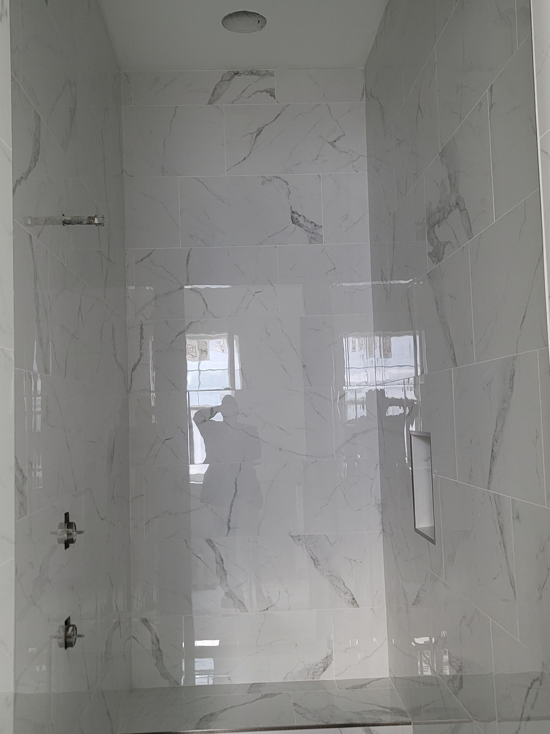 Glossy white tiled shower or bathroom wall with a frosted glass panel and metal handle
