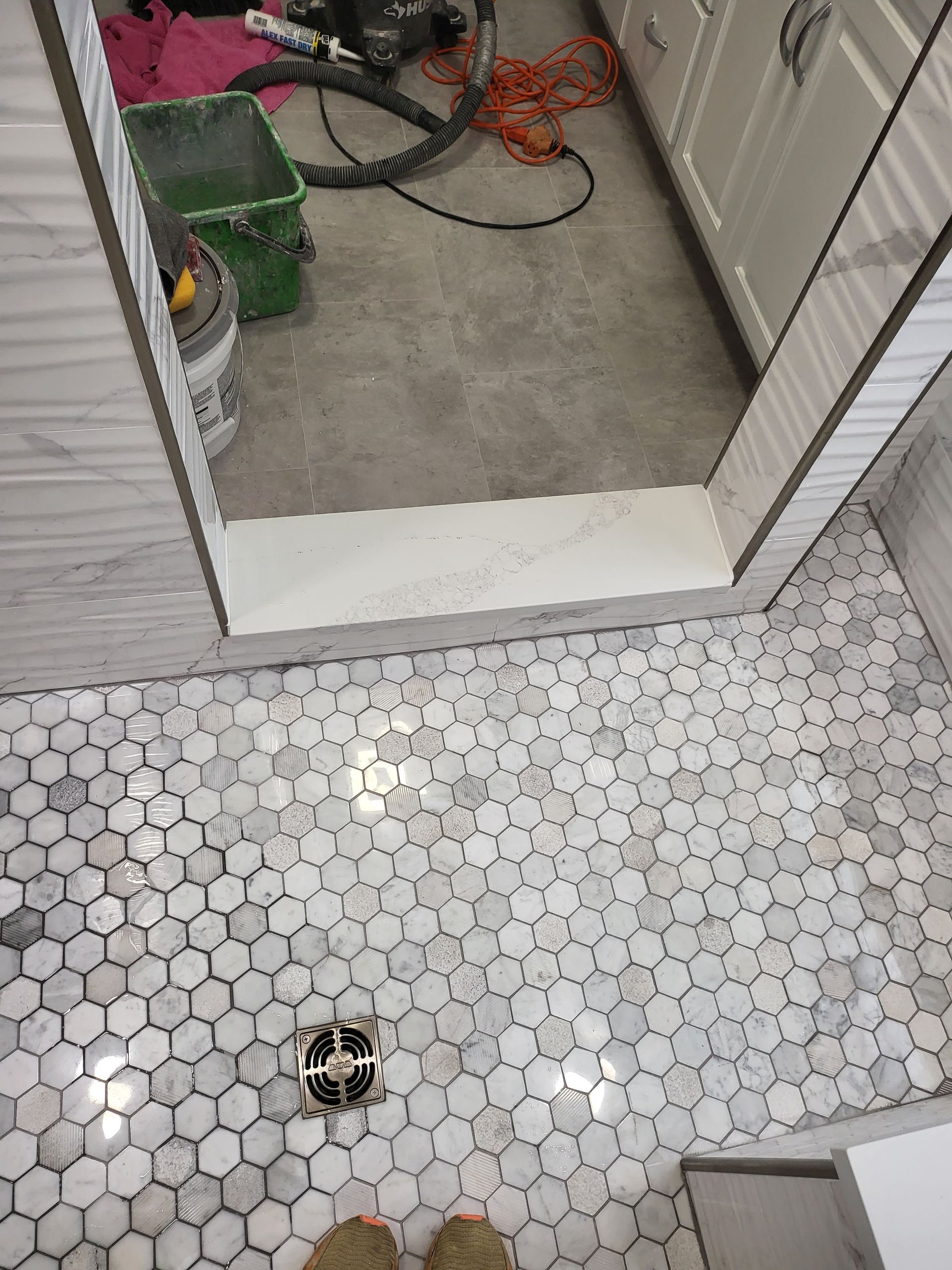 Small tiled bathroom floor with a doorway to a utility area and tools visible beyond.