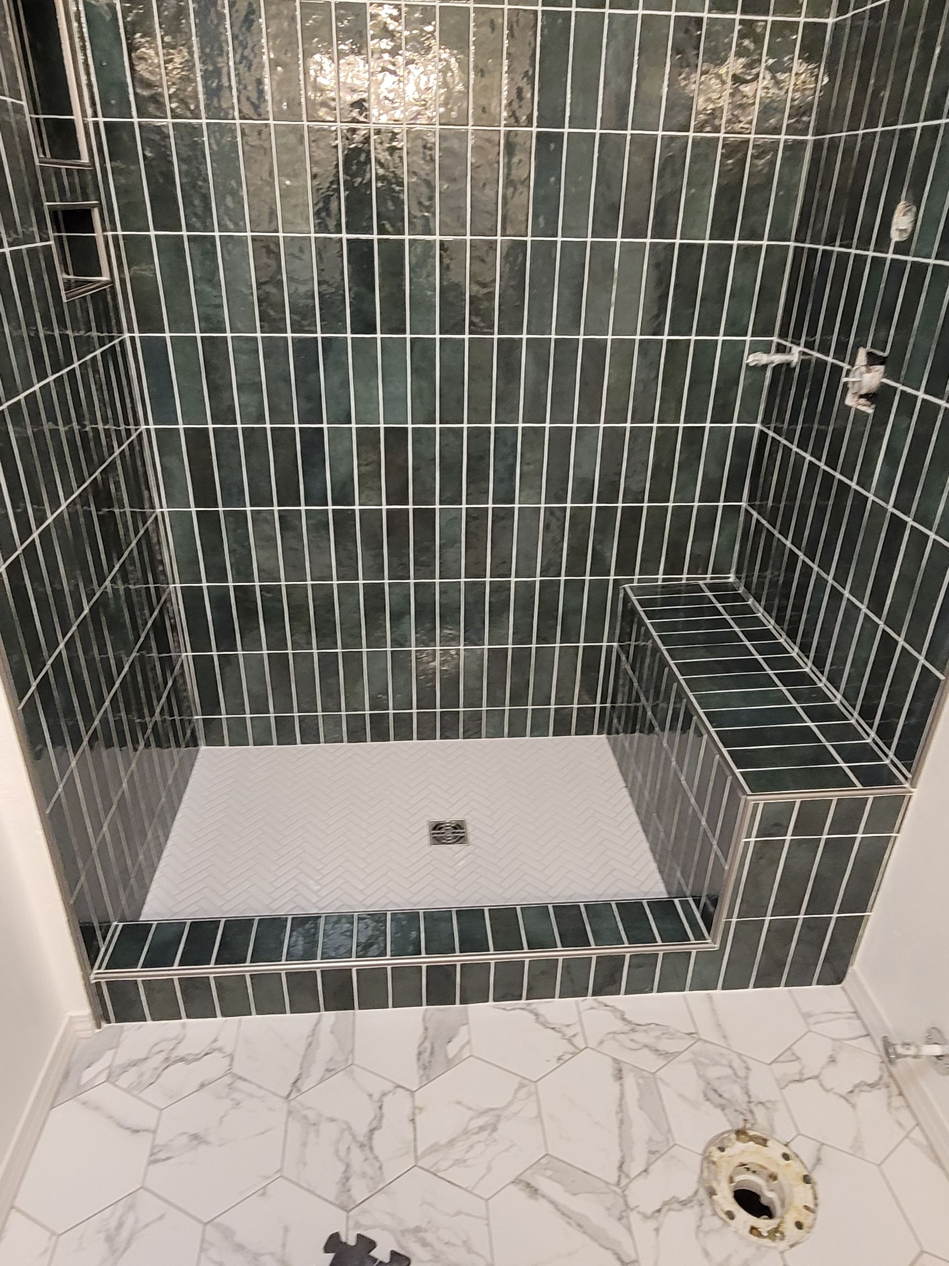 Tiled shower stall with dark green walls, white floor, built-in bench, and marble-look tile outside.