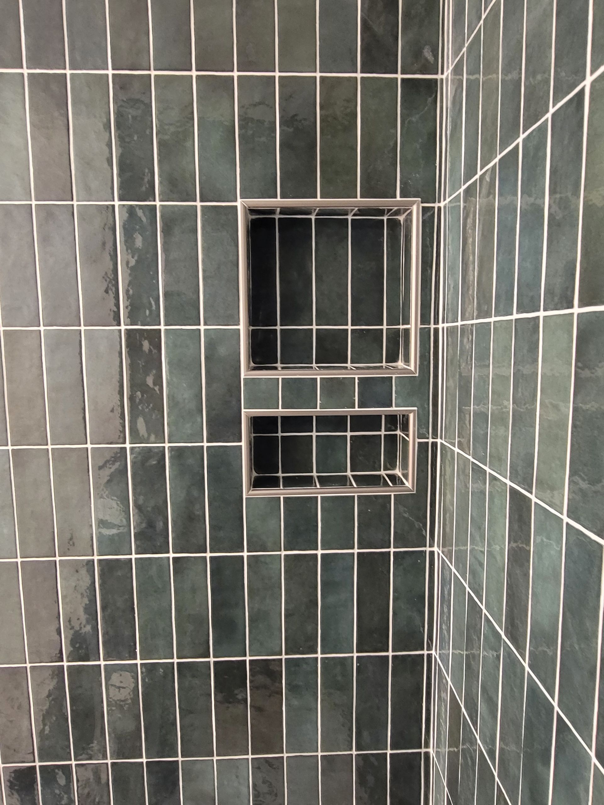 Small tiled shower wall with two recessed shelves and a built-in window opening