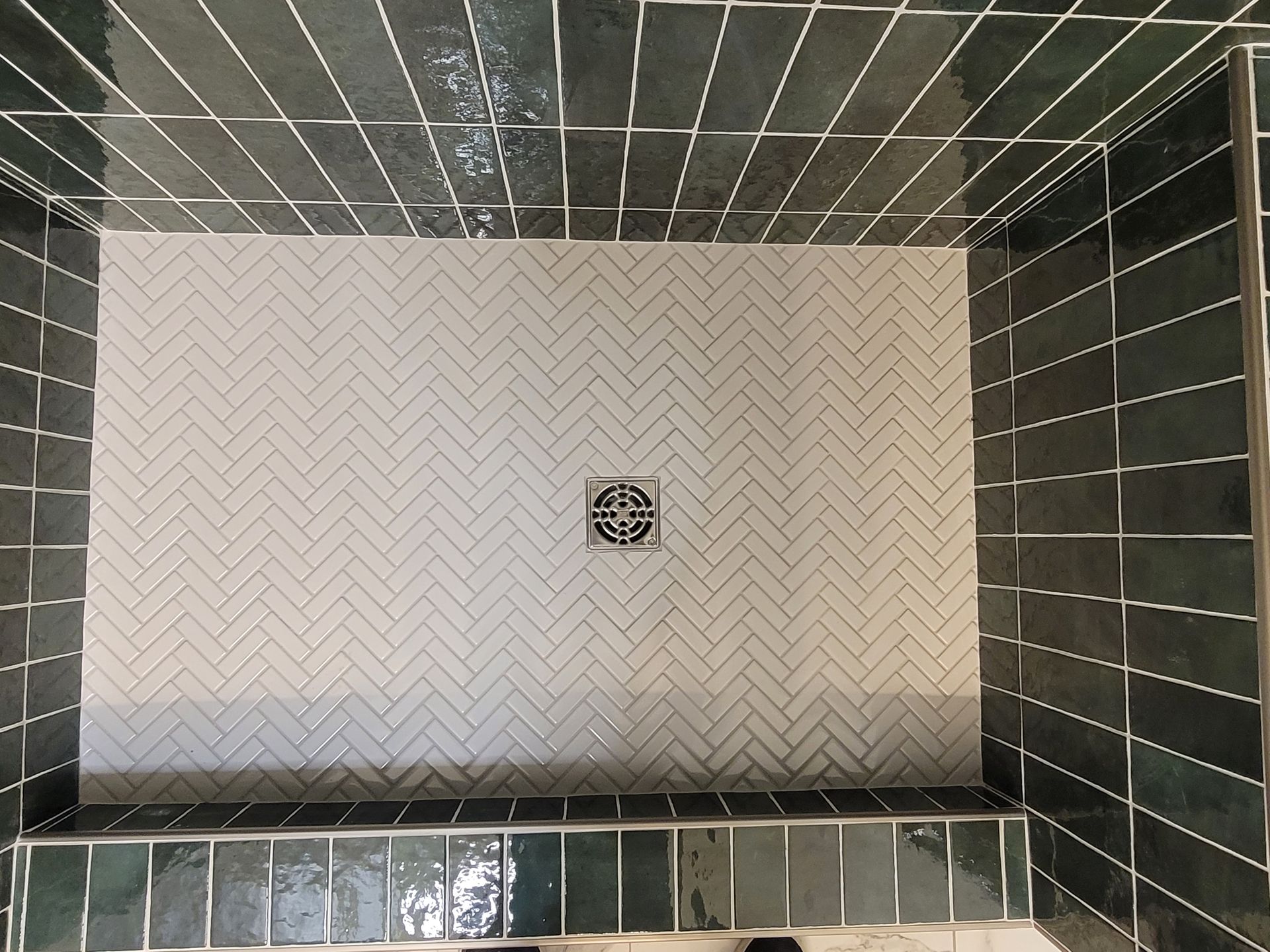 Tiled shower wall with white herringbone center panel and dark green surrounding tiles