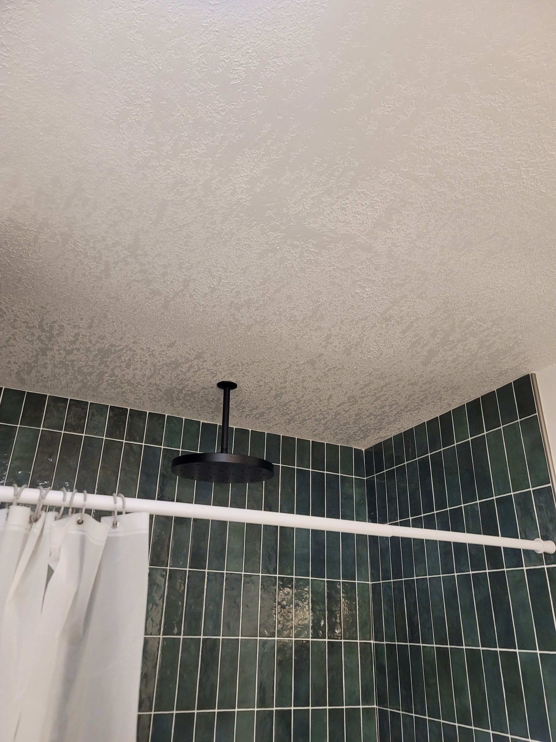 Bathroom corner with green tiled walls, white shower curtain, and a black ceiling light fixture