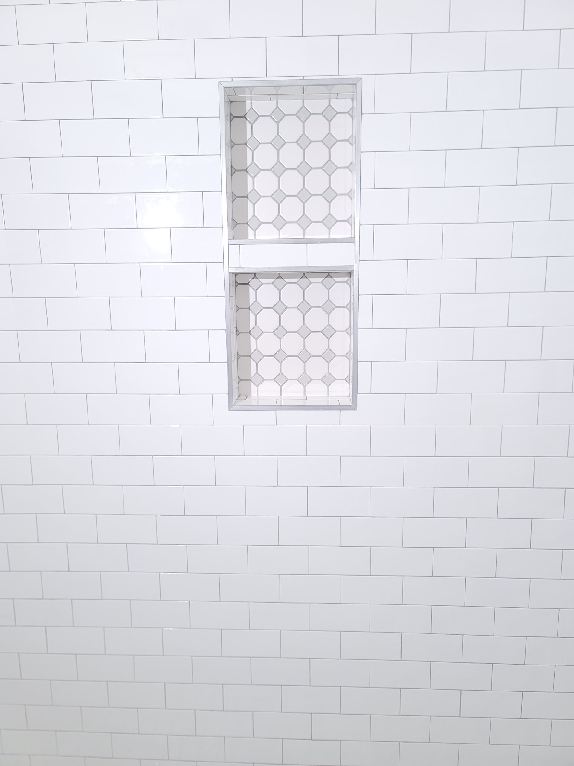 White tiled wall with a small recessed window covered by a patterned metal grille