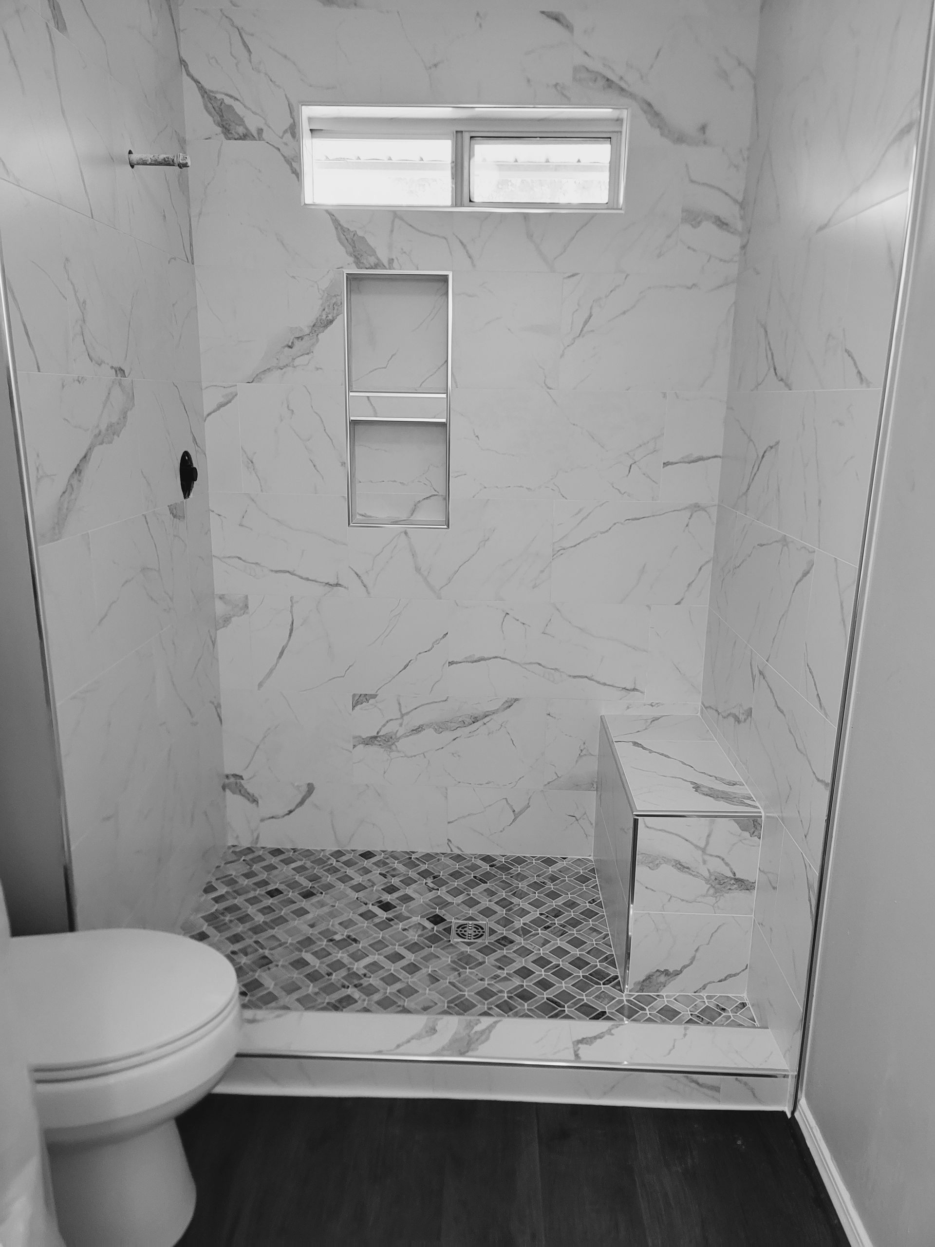 Small tiled bathroom with a toilet, shower area, and small window above the shower.