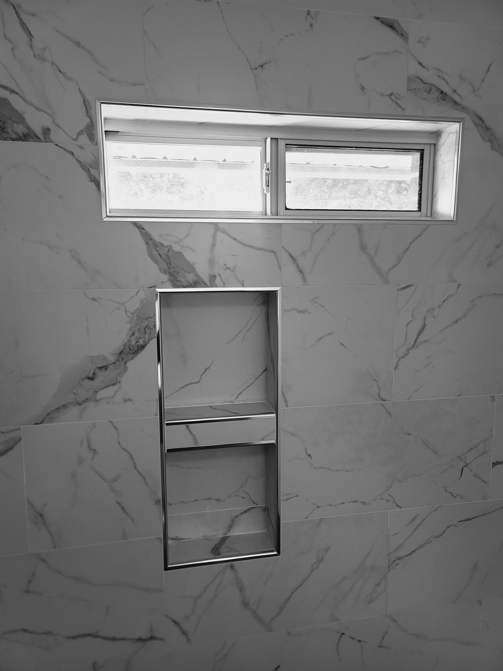 Gray tiled wall with a narrow horizontal window and a rectangular recessed opening below it.