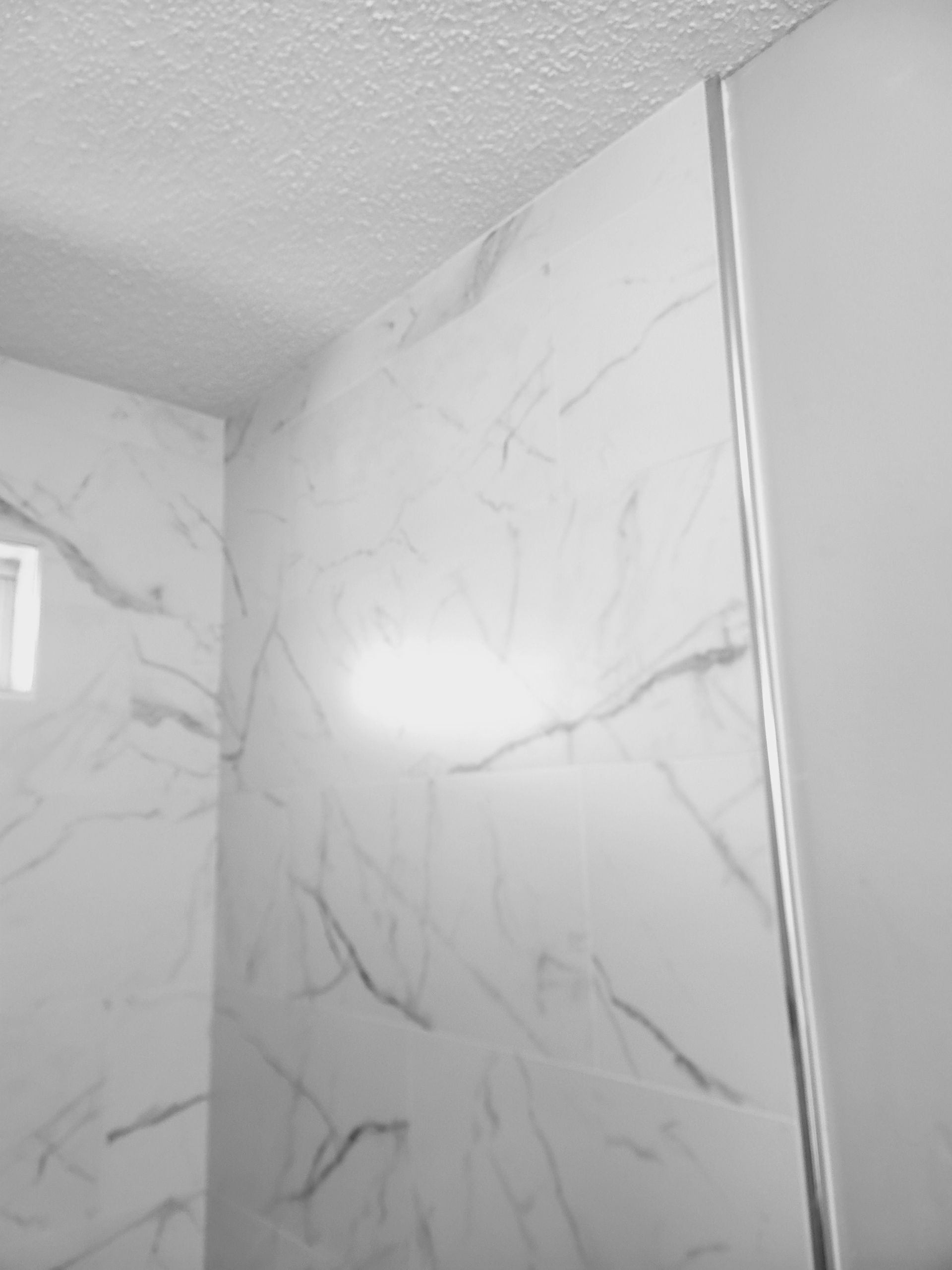 White marble-pattern shower walls and ceiling with a bright light reflection