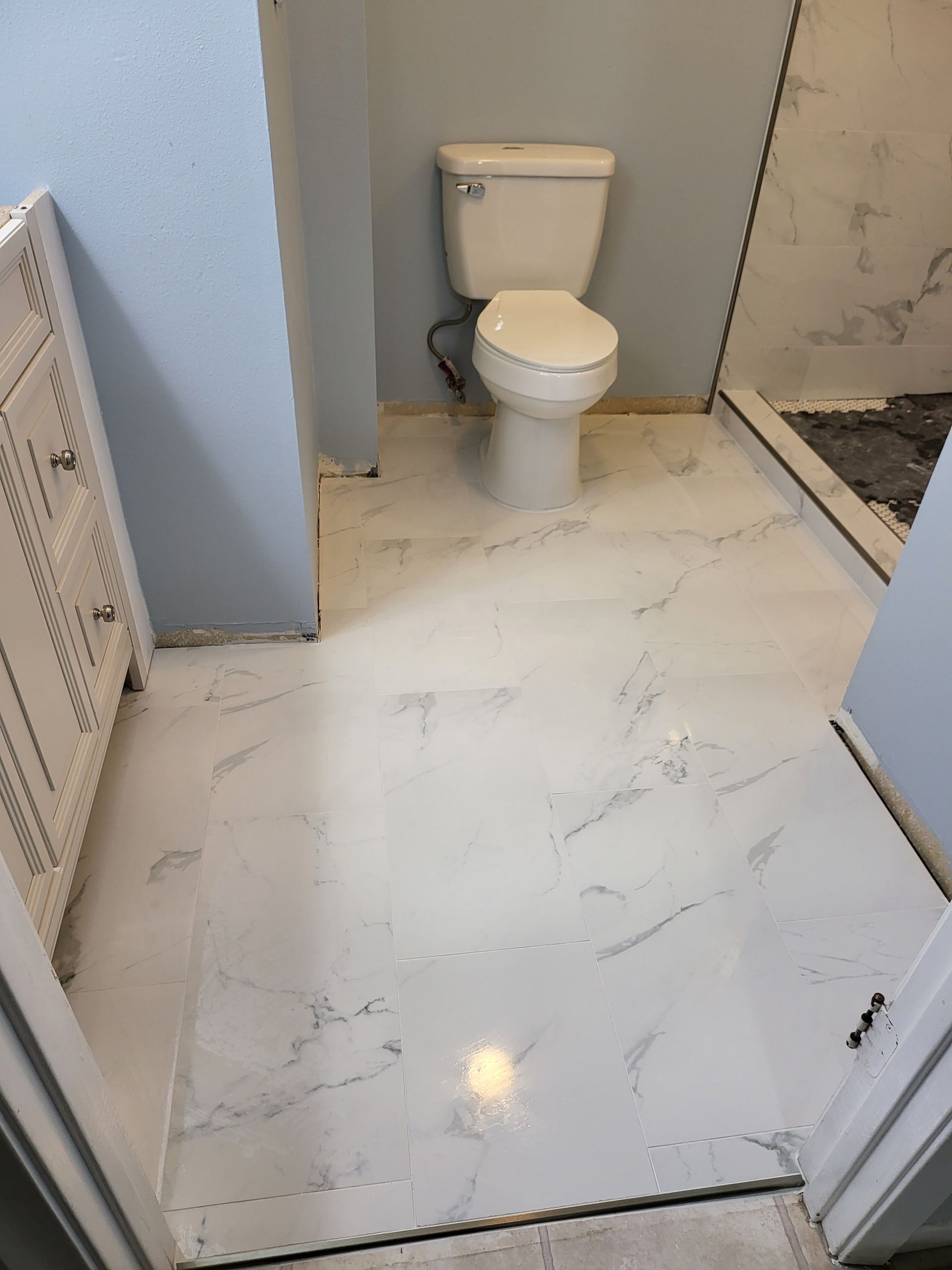 Small bathroom with white tiled floor, toilet, and shower area under construction.