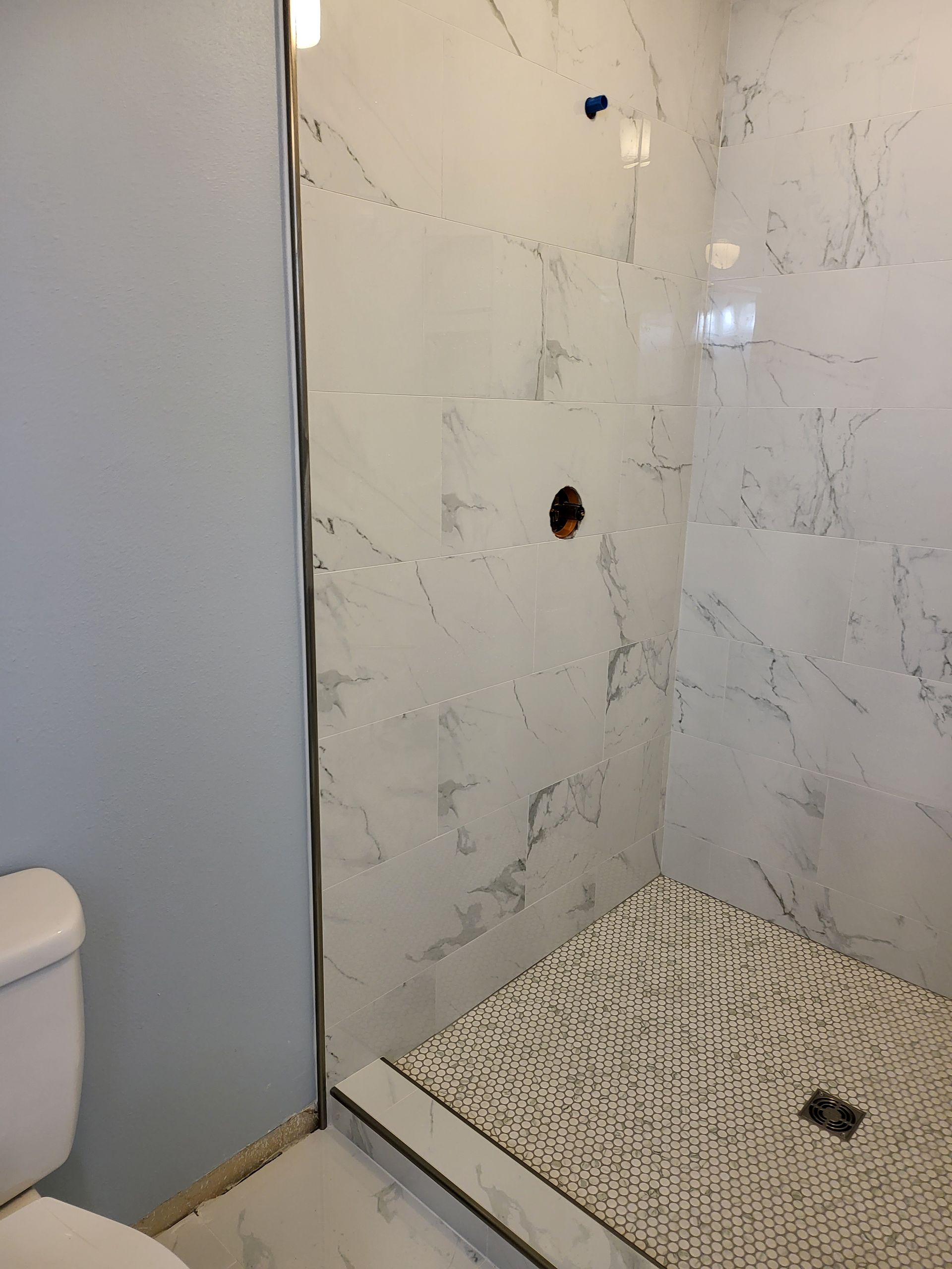 Empty tiled shower stall with a built-in seat and two plumbing holes in the wall.