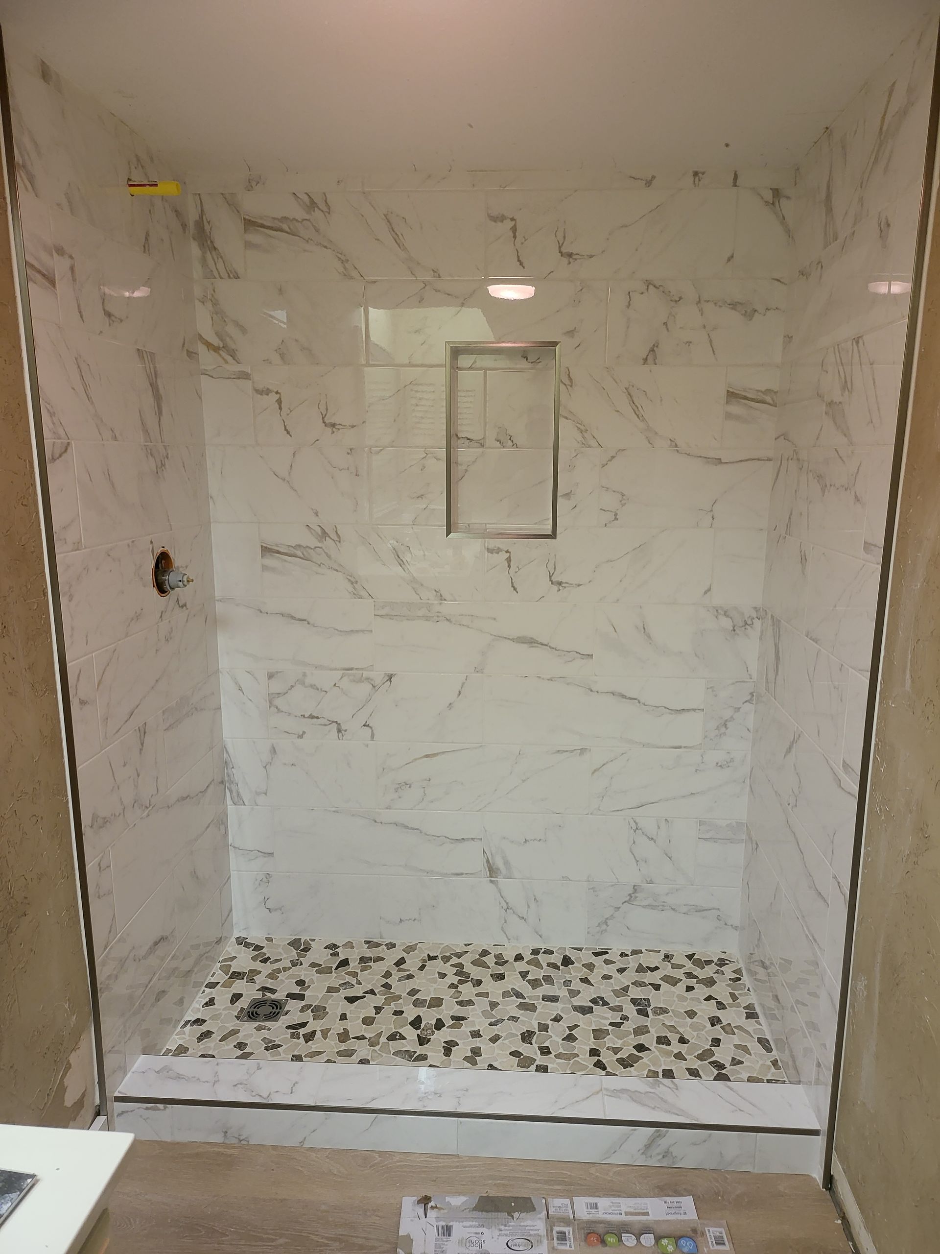 Empty marble-tiled shower stall with a pebble shower floor and recessed shelf