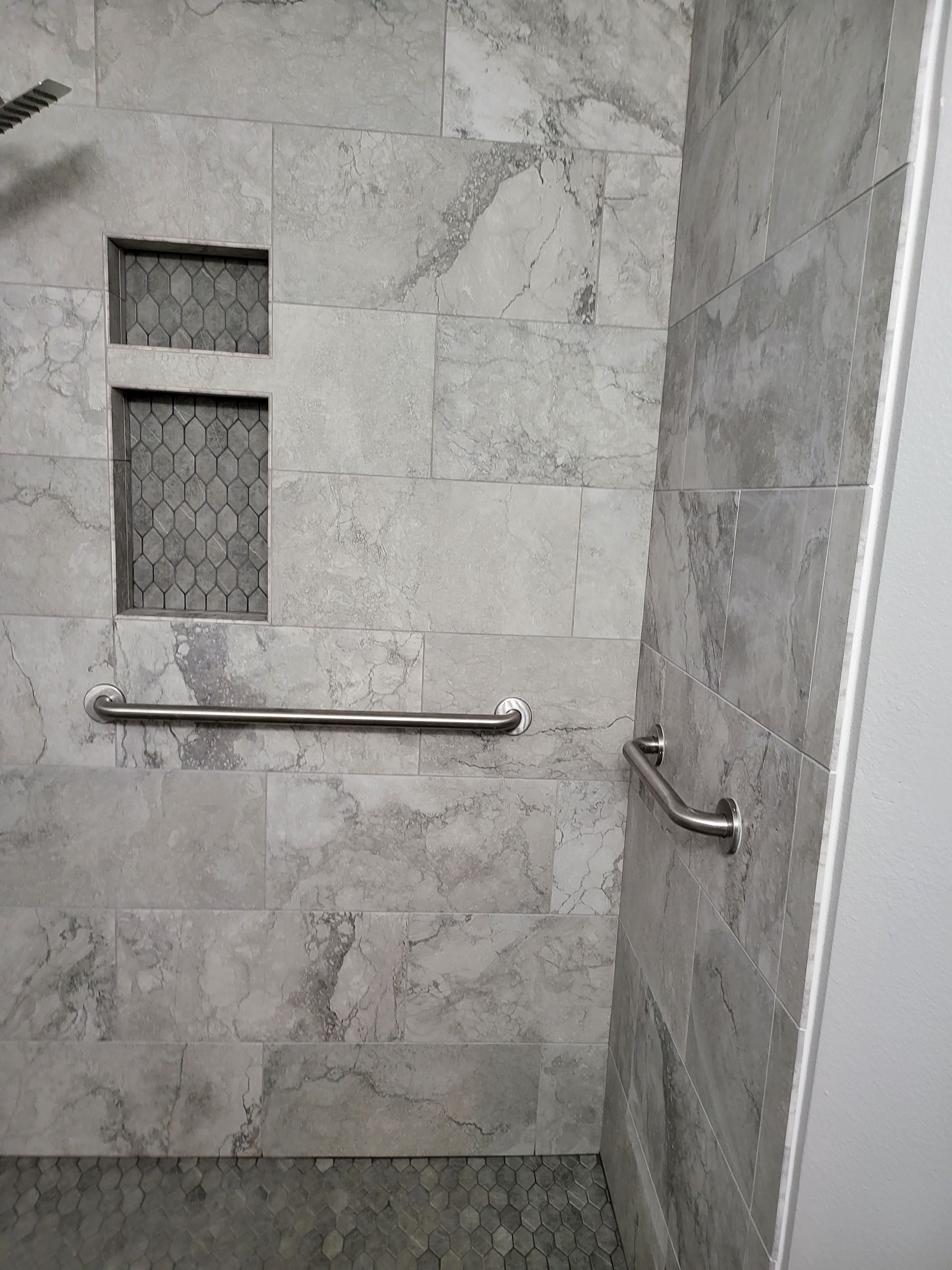 Gray tiled shower with a small frosted window and stainless steel grab bars.