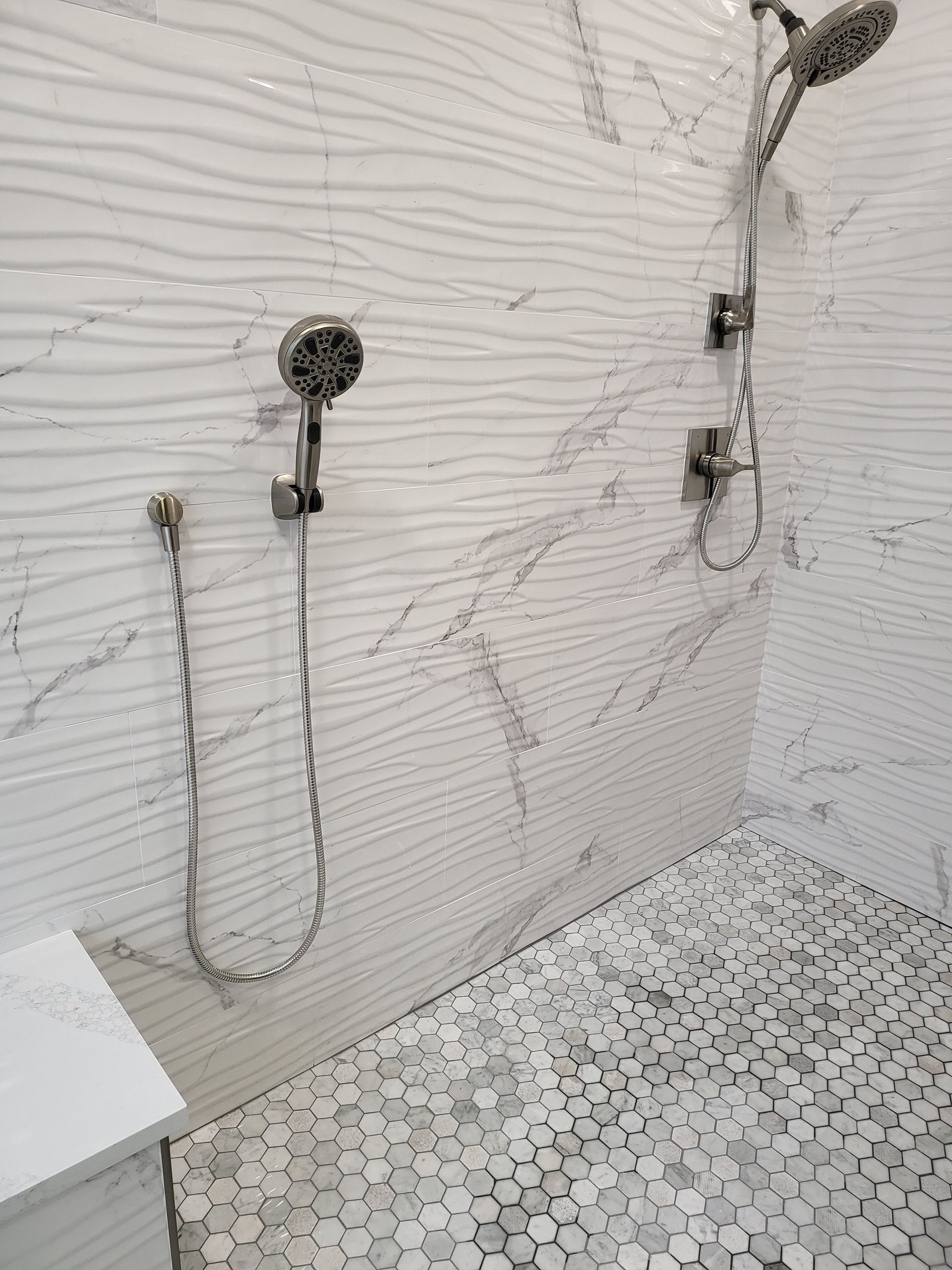 Modern tiled bathroom wall with exposed shower fixtures and white mosaic floor tiles