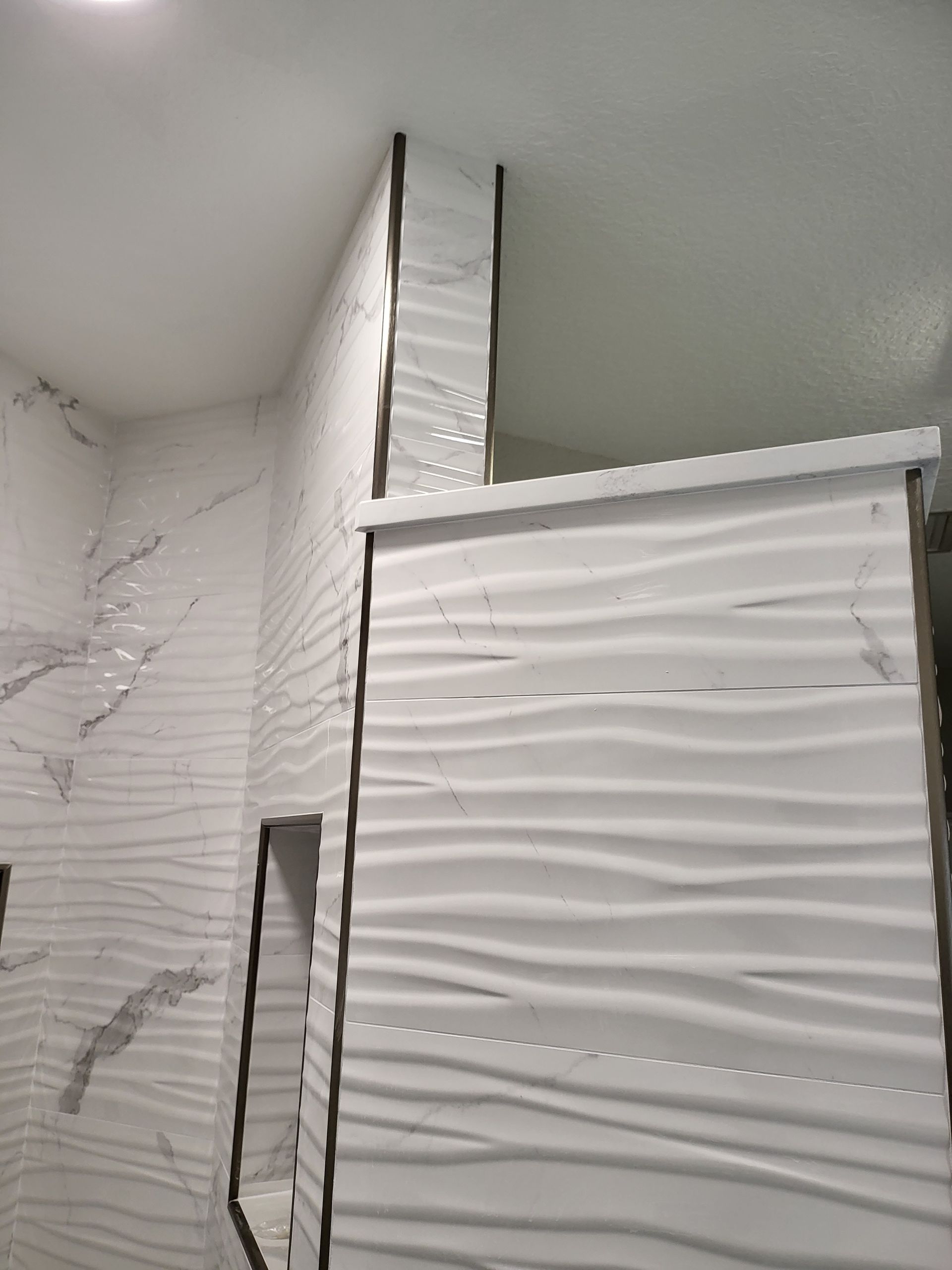 White textured shower walls and a glass shower door in a bathroom corner