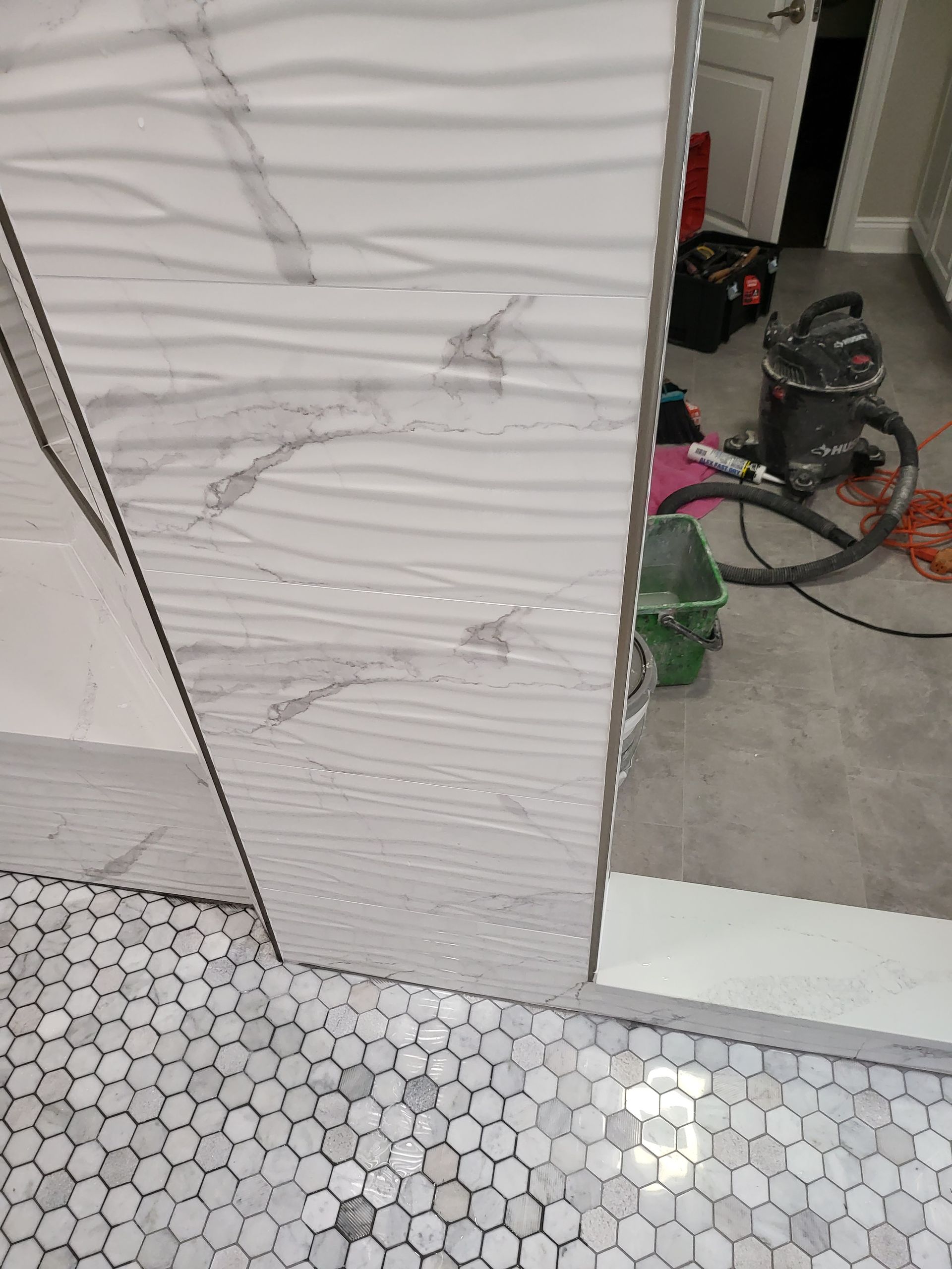 Damaged white wall tile with cracks and dents beside a mirror, in a bathroom or utility room