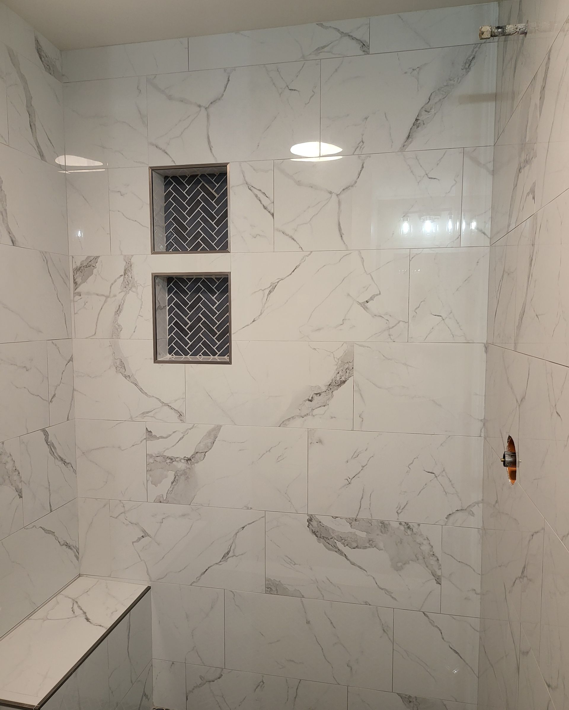 White marble-tiled shower stall with two small diamond-pattern windows and a built-in corner shelf.