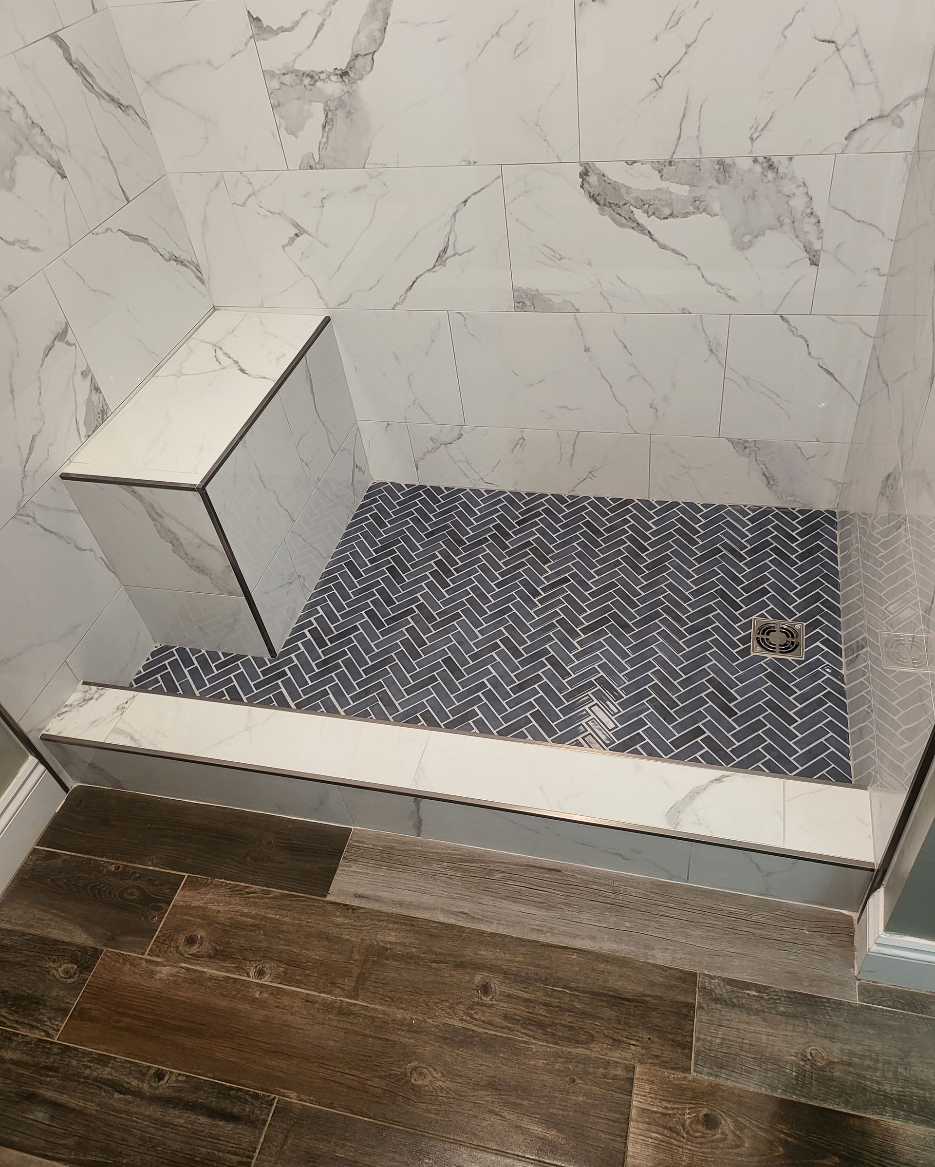 Tiled walk-in shower with blue mosaic floor, marble-look walls, and a white bench