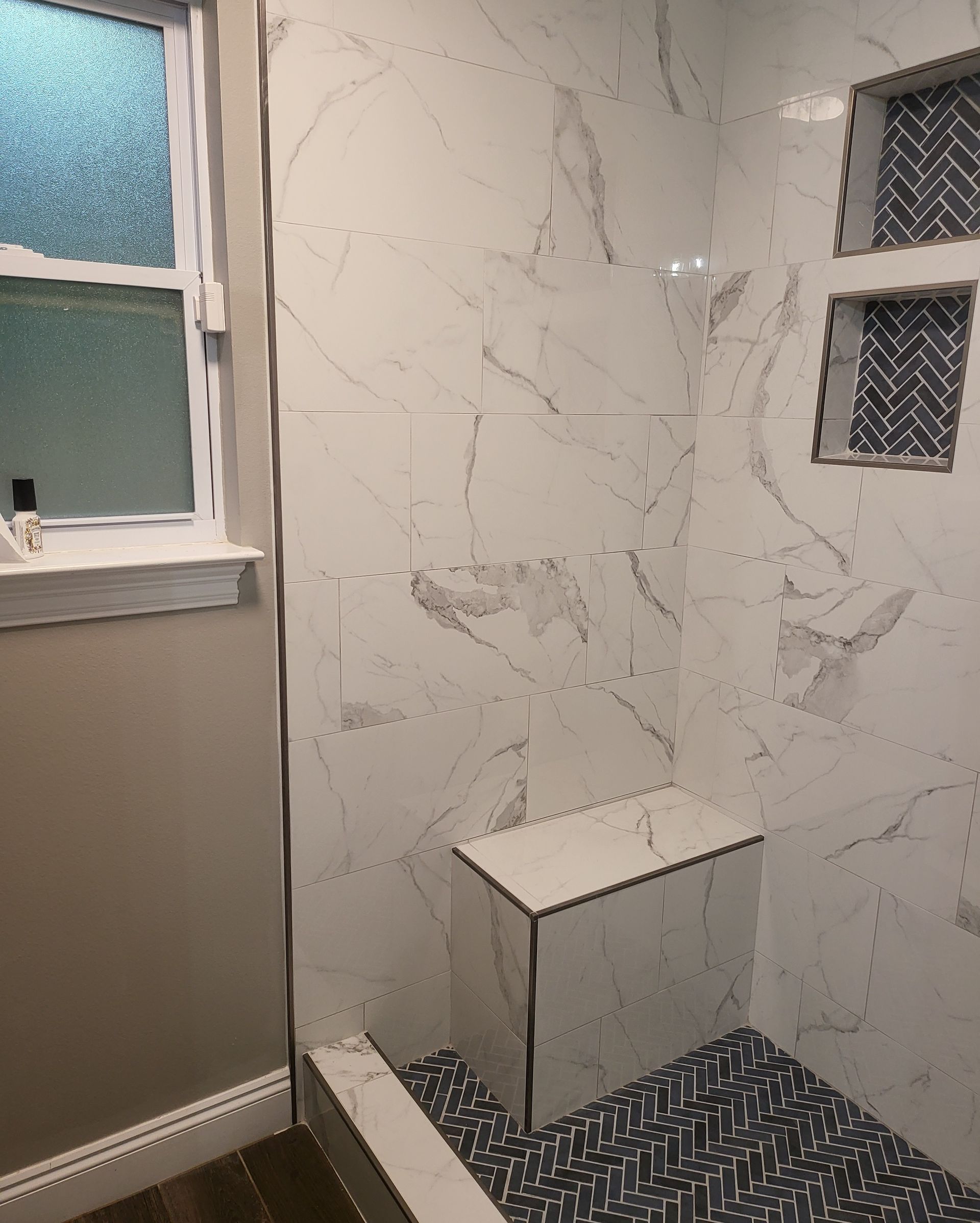 Small bathroom with marble-look shower wall, small bench, and frosted window.