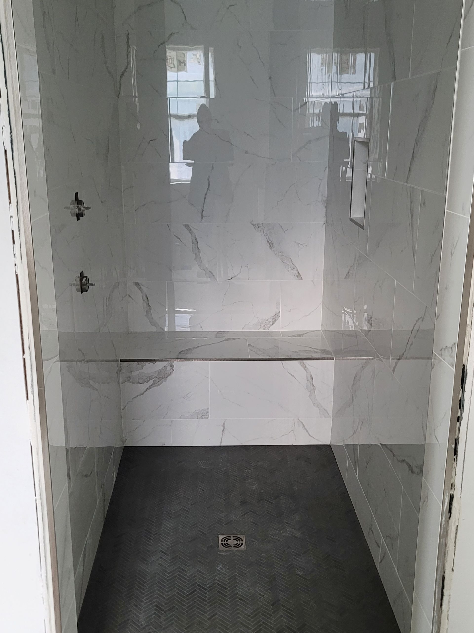 Empty tiled shower stall with gray floor and white marble-pattern walls.