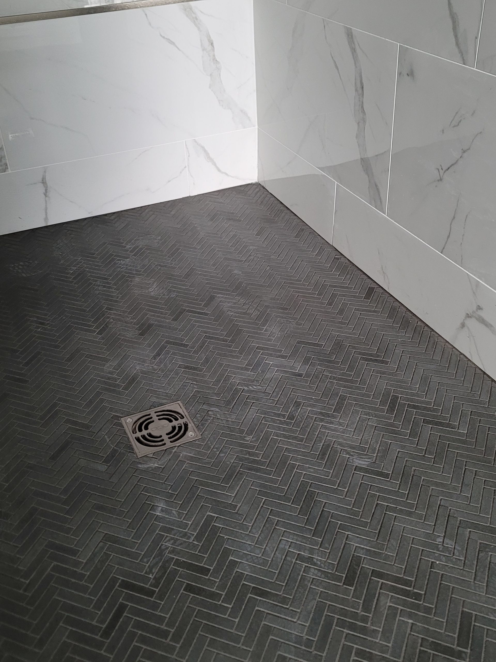 Tiled shower corner with a dark herringbone floor and a circular drain