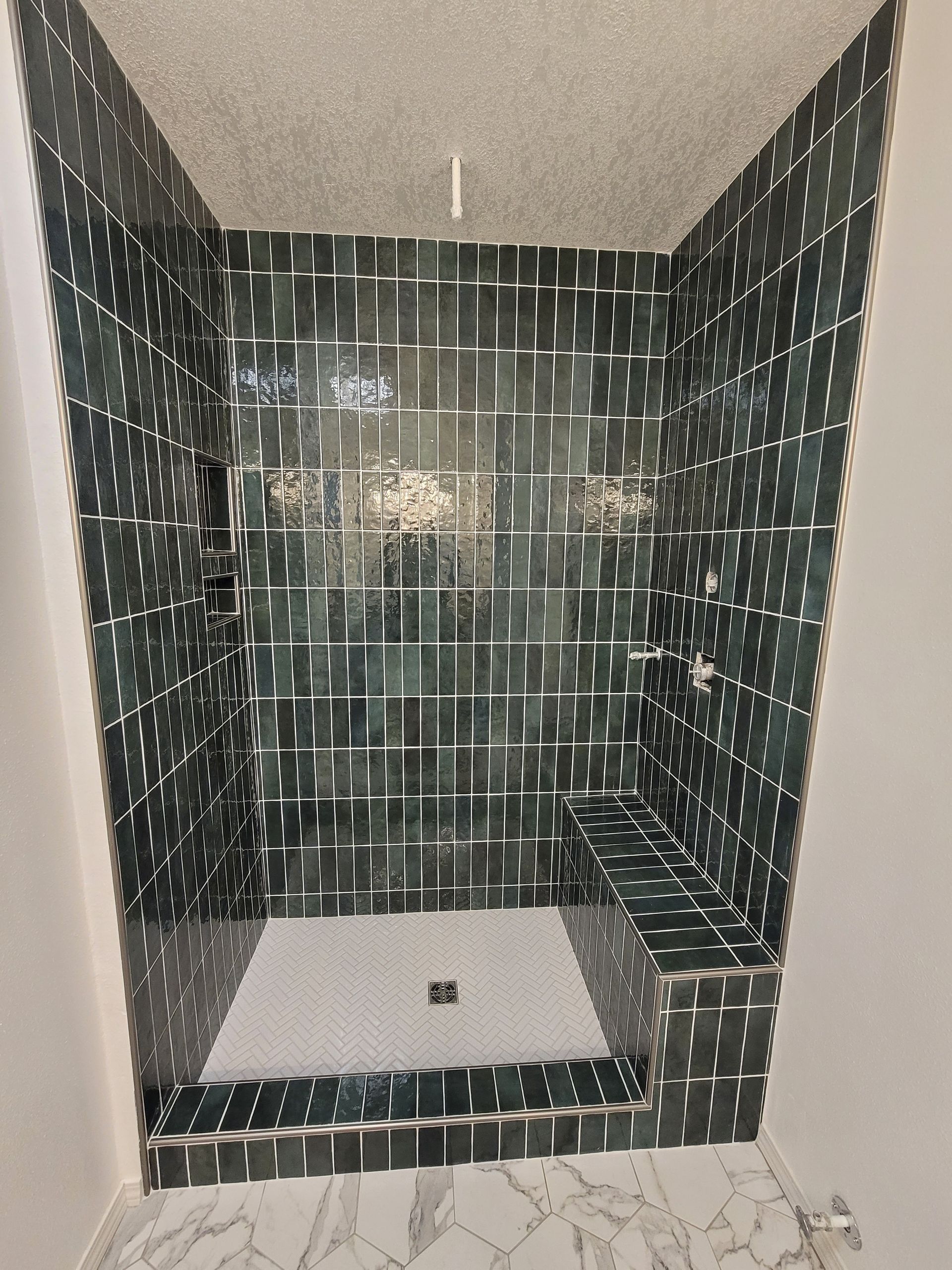 Tiled walk-in shower with dark mosaic walls, glass door, and white shower pan