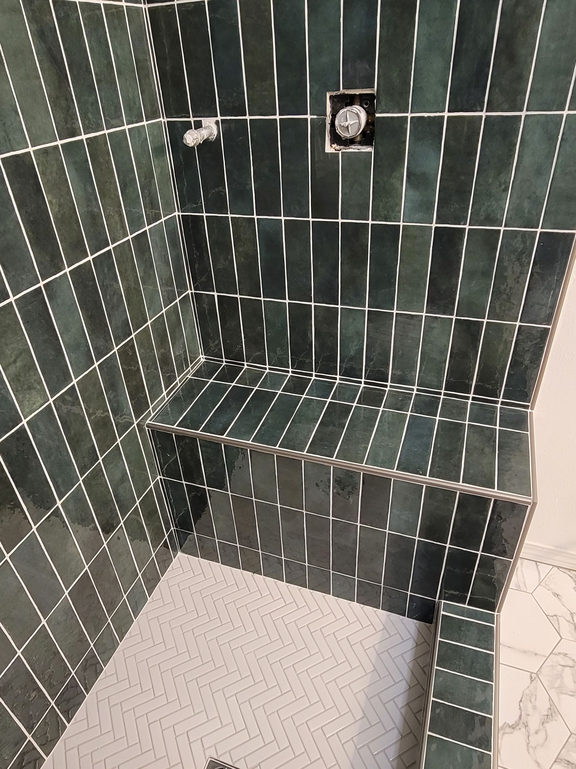 Green-tiled shower stall with a built-in bench and white mosaic floor