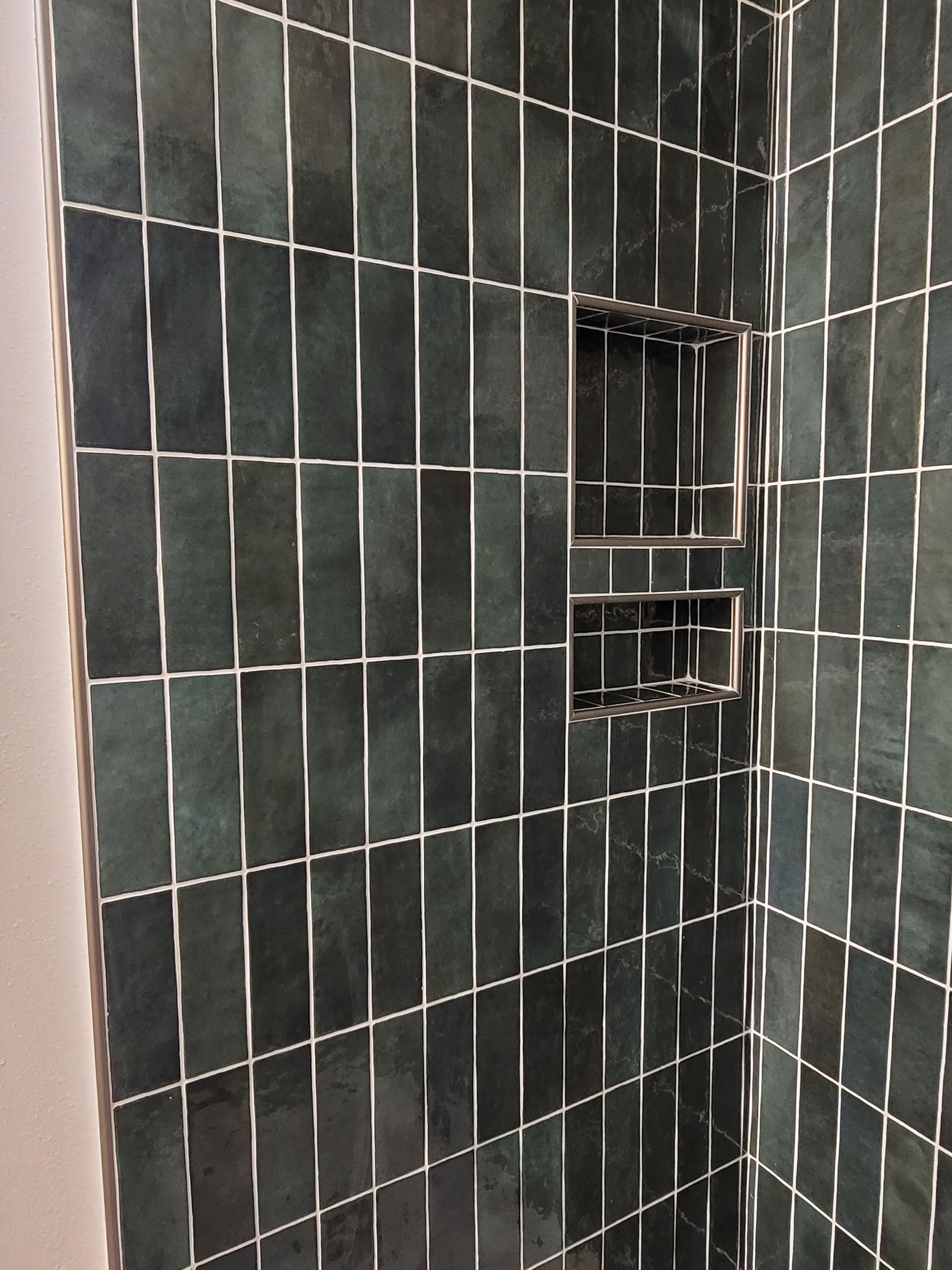 Green tiled shower corner with a small built-in shelf and chrome fixtures