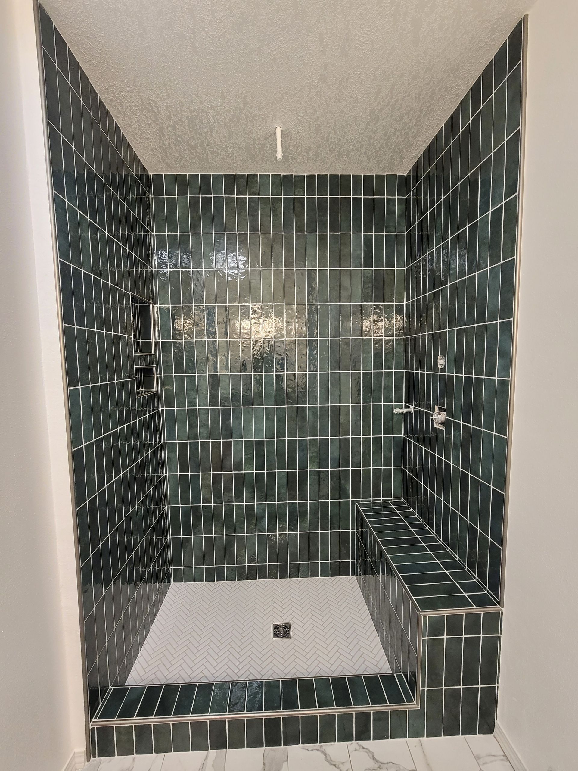 Dark green tiled shower with built-in bench and white shower pan, viewed from the doorway
