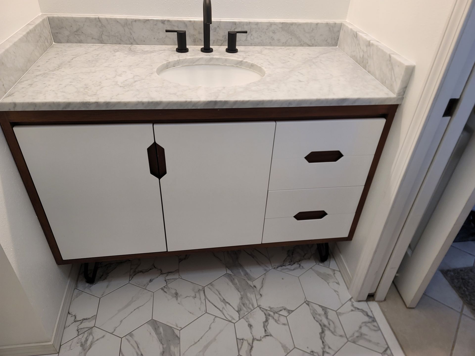 Modern bathroom vanity with light stone countertop, black faucet, and marble-pattern tile floor