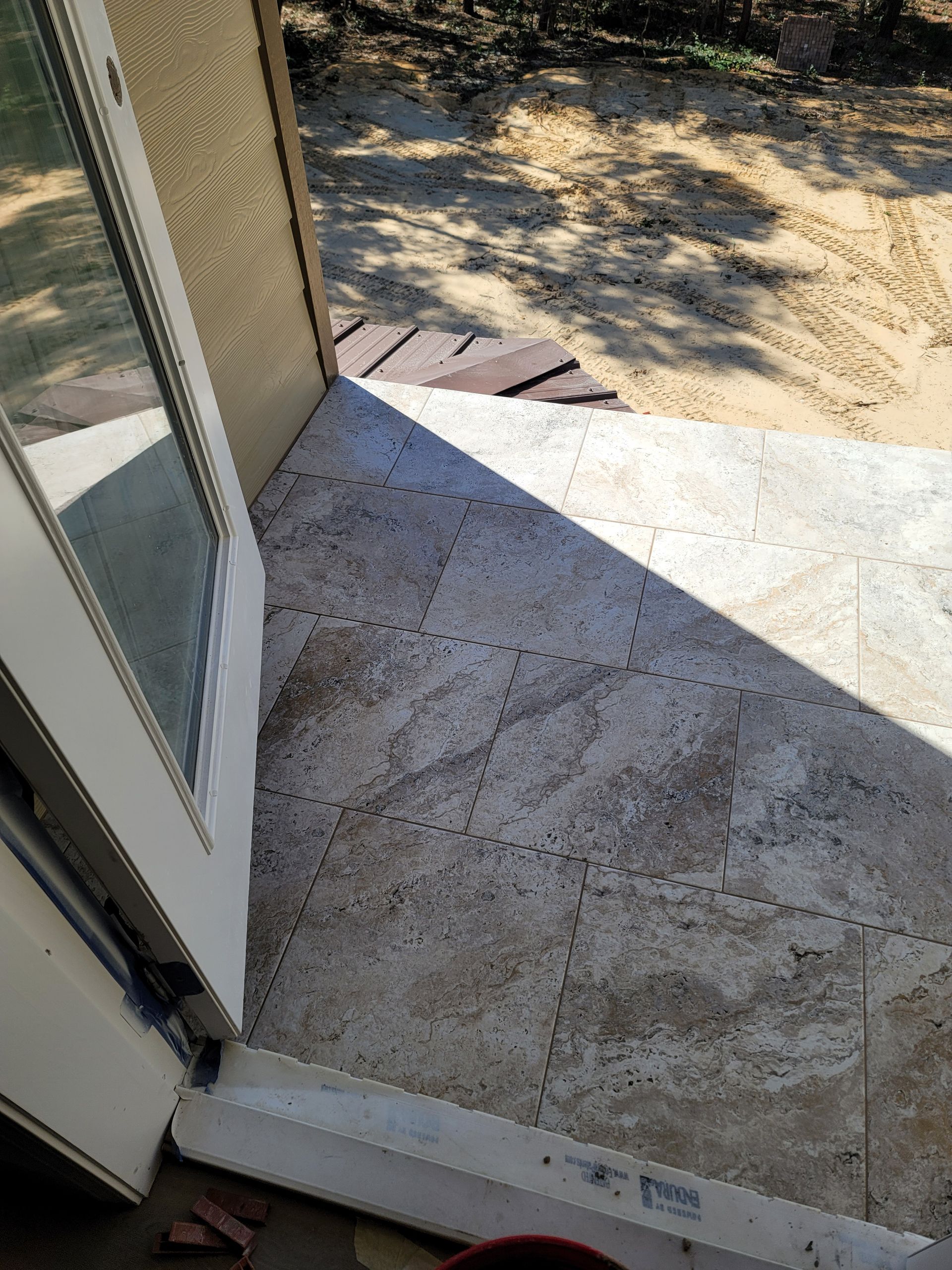 Open doorway to a sunlit concrete patio with dirt yard beyond.