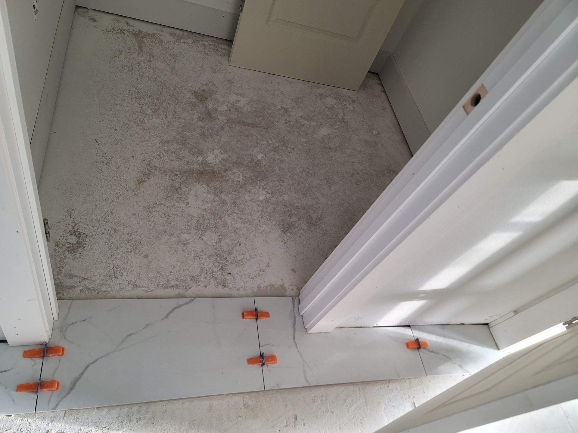 Hallway threshold with cracked white tile and a dirty carpeted room beyond