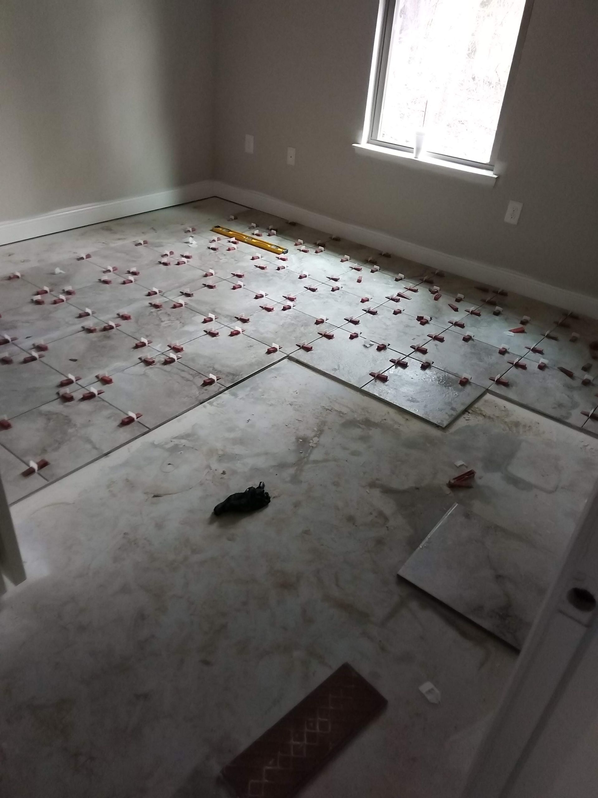 Empty room with bare floor, debris scattered near a window, and a few floor tiles and boards lying around.